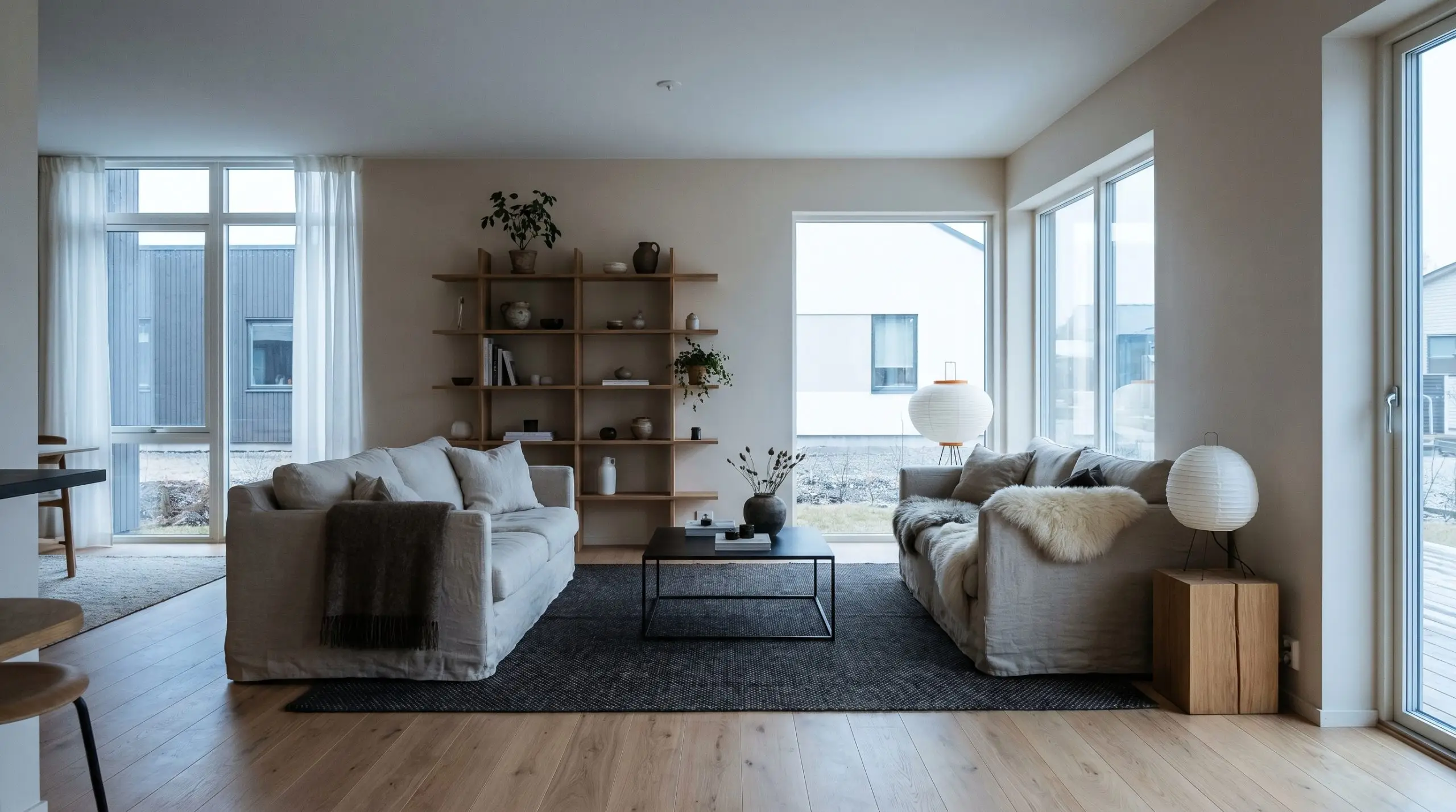 A low-profile washed linen slipcovered sofa sits on natural white oak flooring alongside a blackened steel coffee table and a dark charcoal geometric rug.