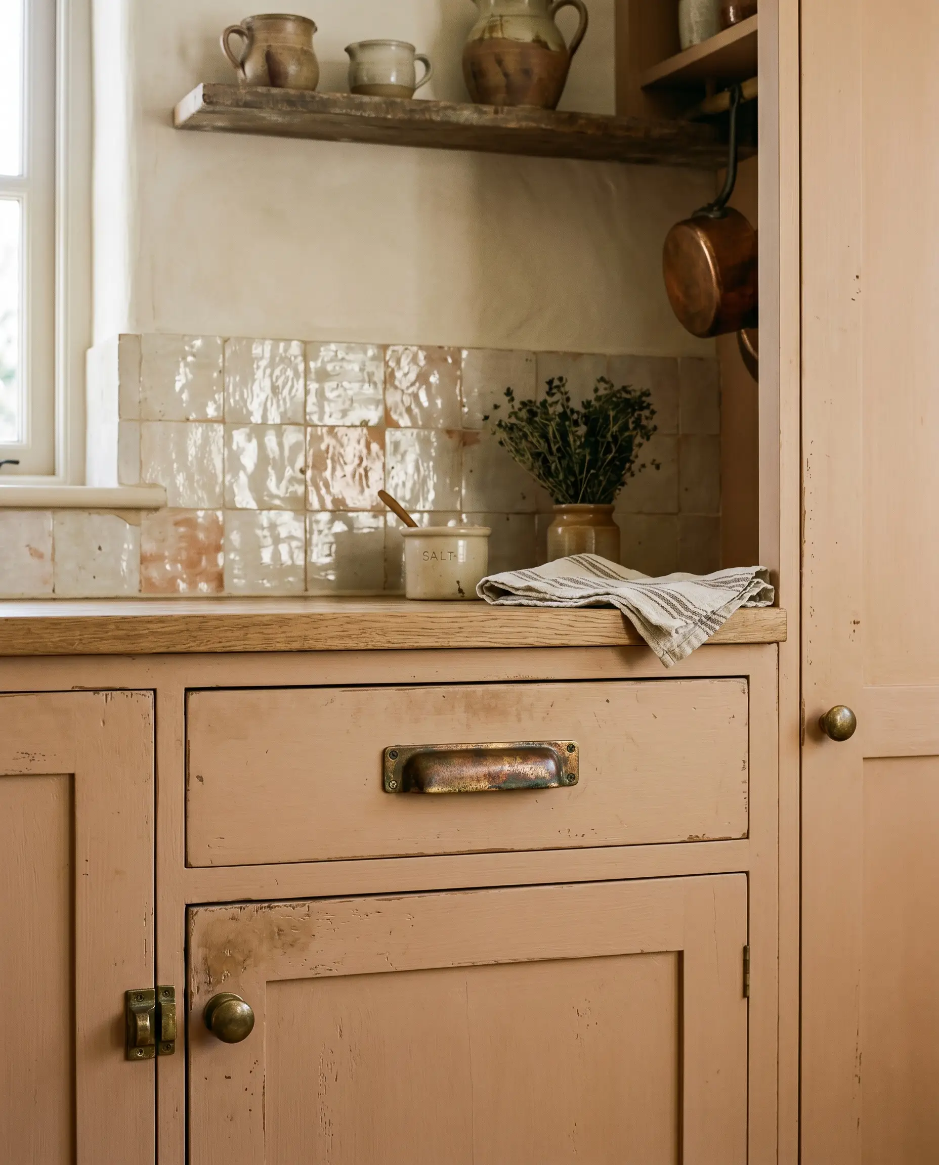 Solid unlacquered brass pulls and knobs with a living patina complement the terracotta base bleeding through a perfectly imperfect undulating glossy tile wall.