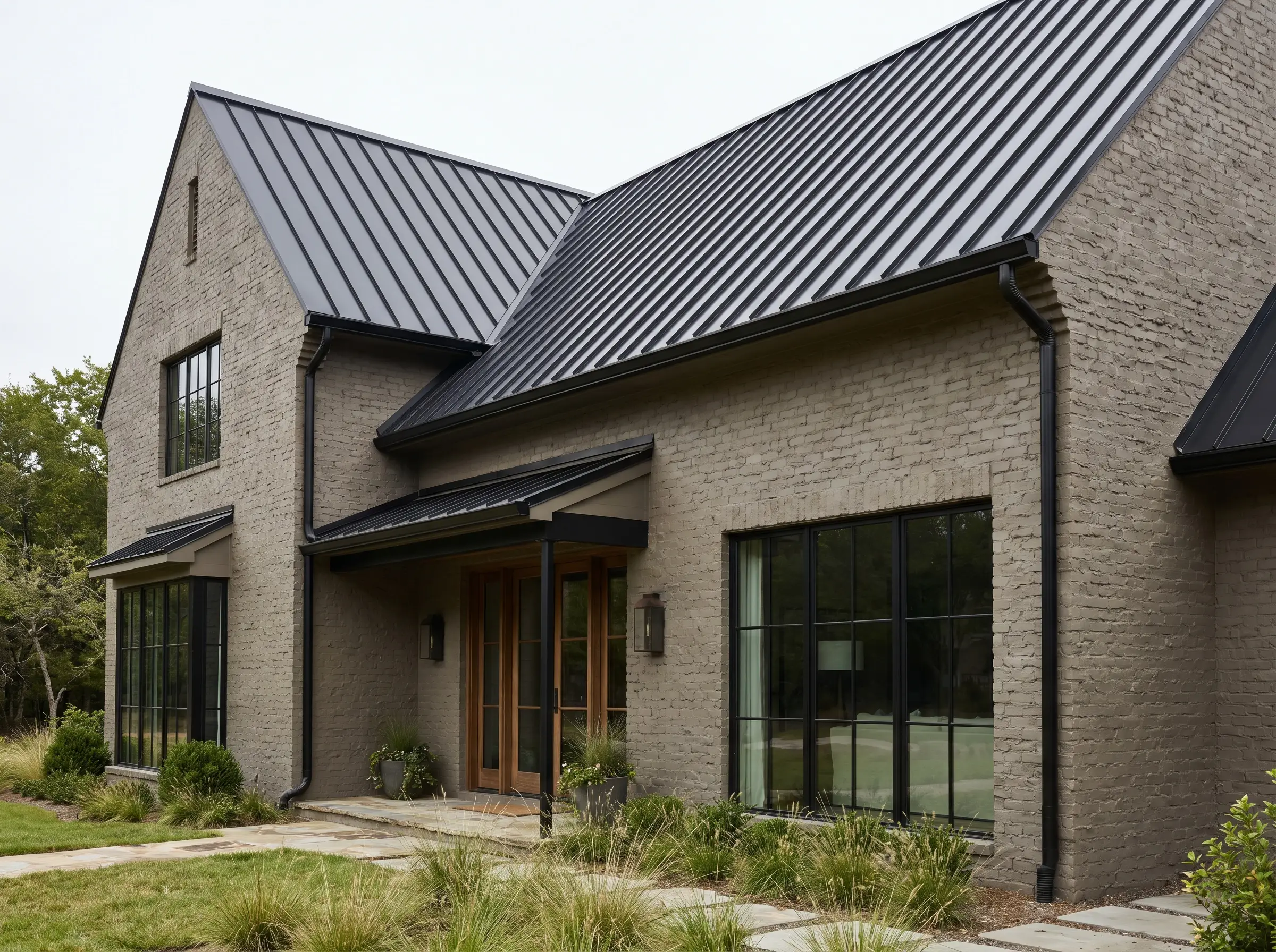 A striking matte black standing seam metal roof and matching gutters cap an earthy painted brick structure showcasing modern greige facade ideas.