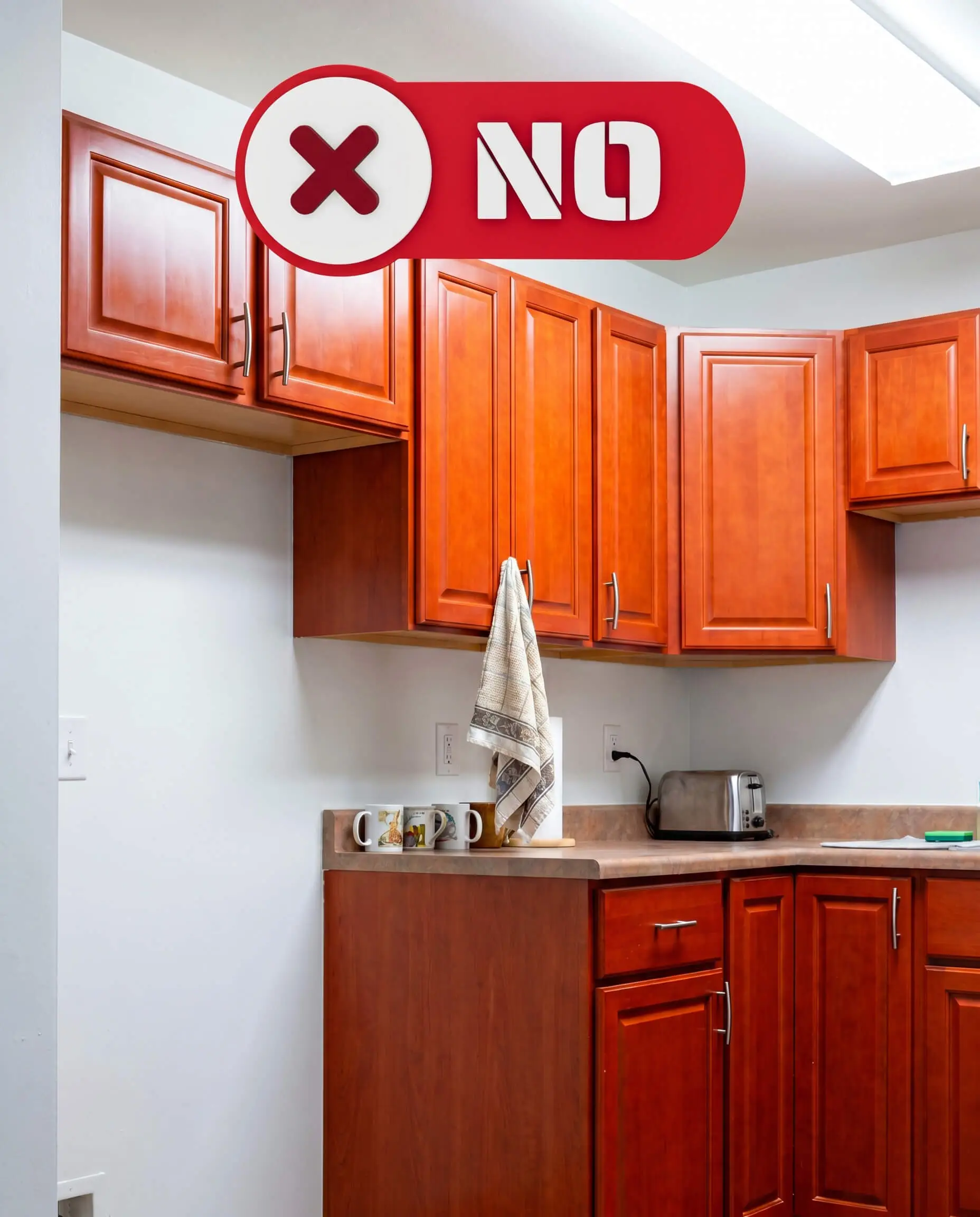 Pure stark builder-grade white walls create an aggressive visual contrast against intensely orange-red cherry wood cabinets equipped with basic hardware.