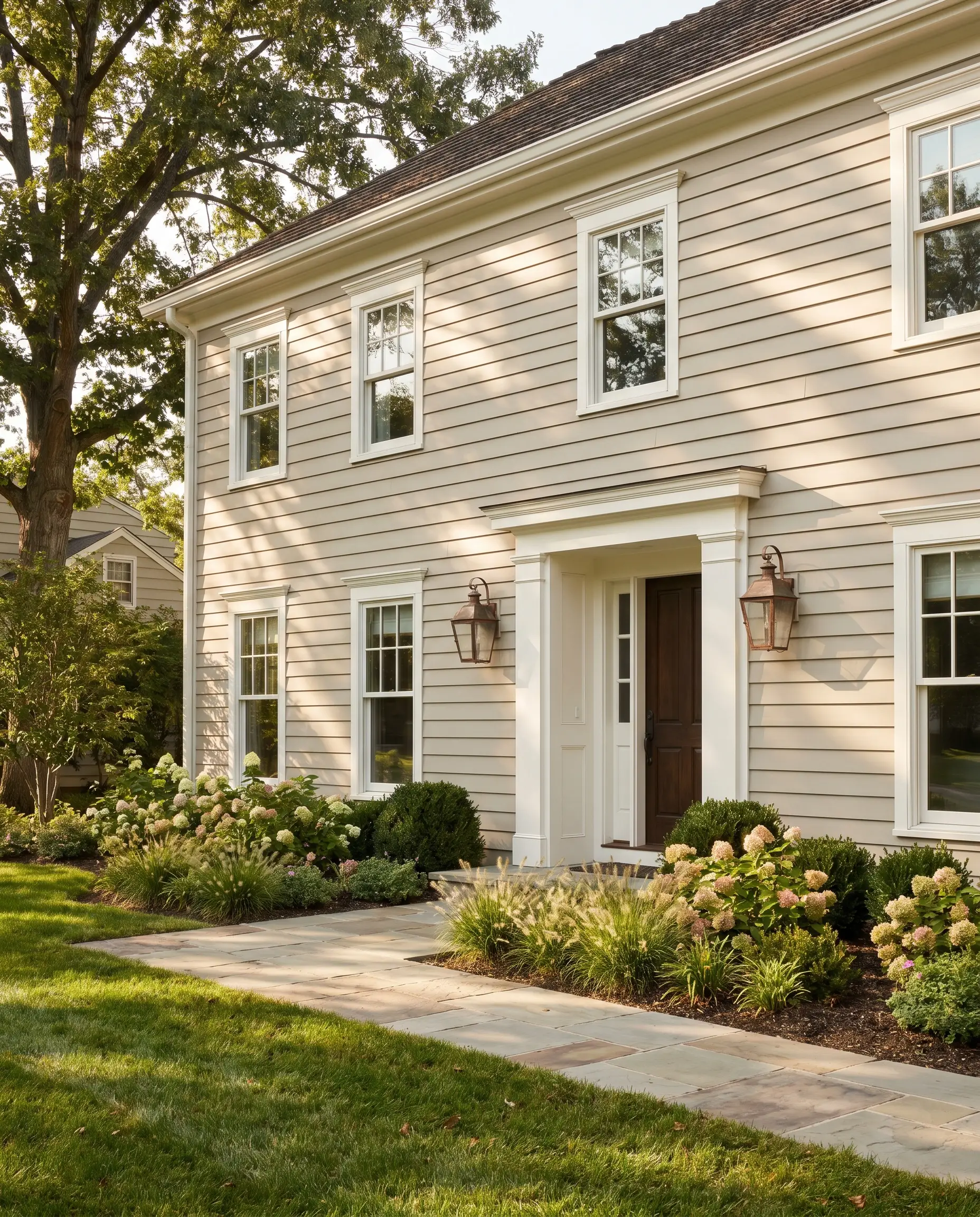 Soft transitional greige exterior siding contrasts with crisp sharp white trim and traditional copper lighting fixtures on a new traditional home.