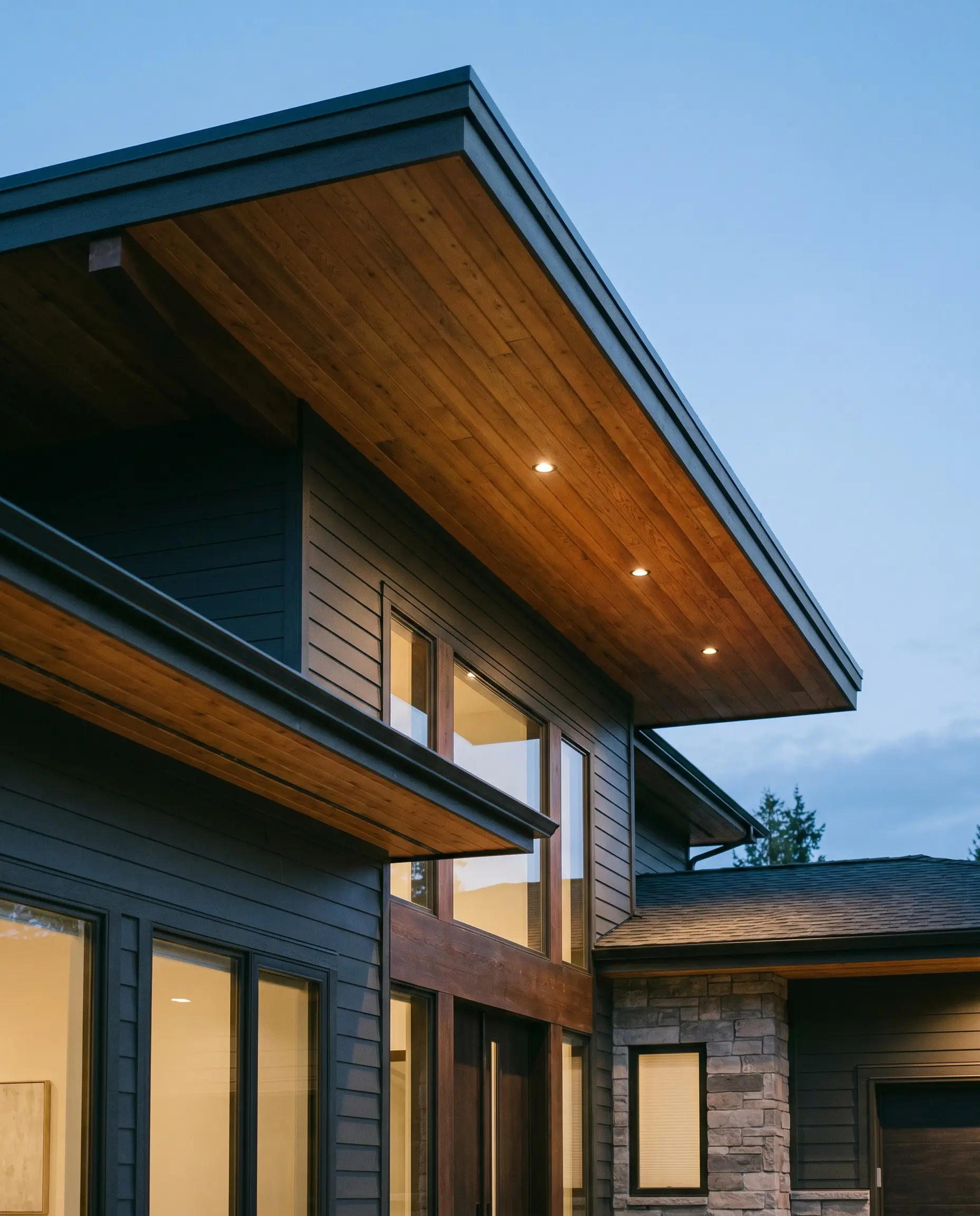 Deep charcoal satin-finish siding contrasts against an exposed roof overhang lined with clear-sealed, tongue-and-groove natural cedar soffits and recessed LED lighting.