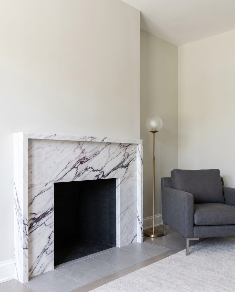 An ultra-thin honed Lilac stone micro-mantel with a four-inch shelf depth and striking purple veining sits near a sleek contemporary armchair and brass floor lamp.