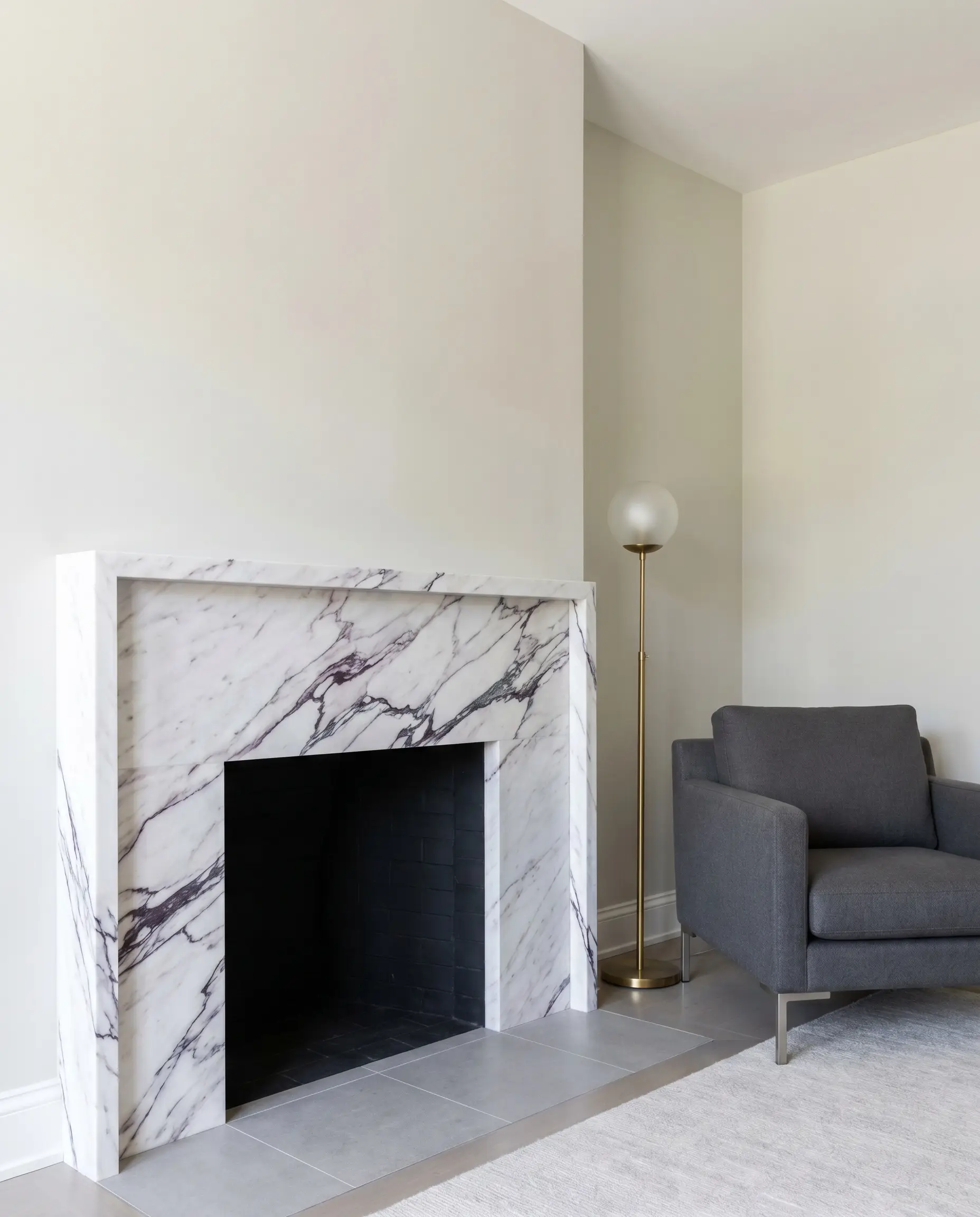An ultra-thin honed Lilac stone micro-mantel with a four-inch shelf depth and striking purple veining sits near a sleek contemporary armchair and brass floor lamp.