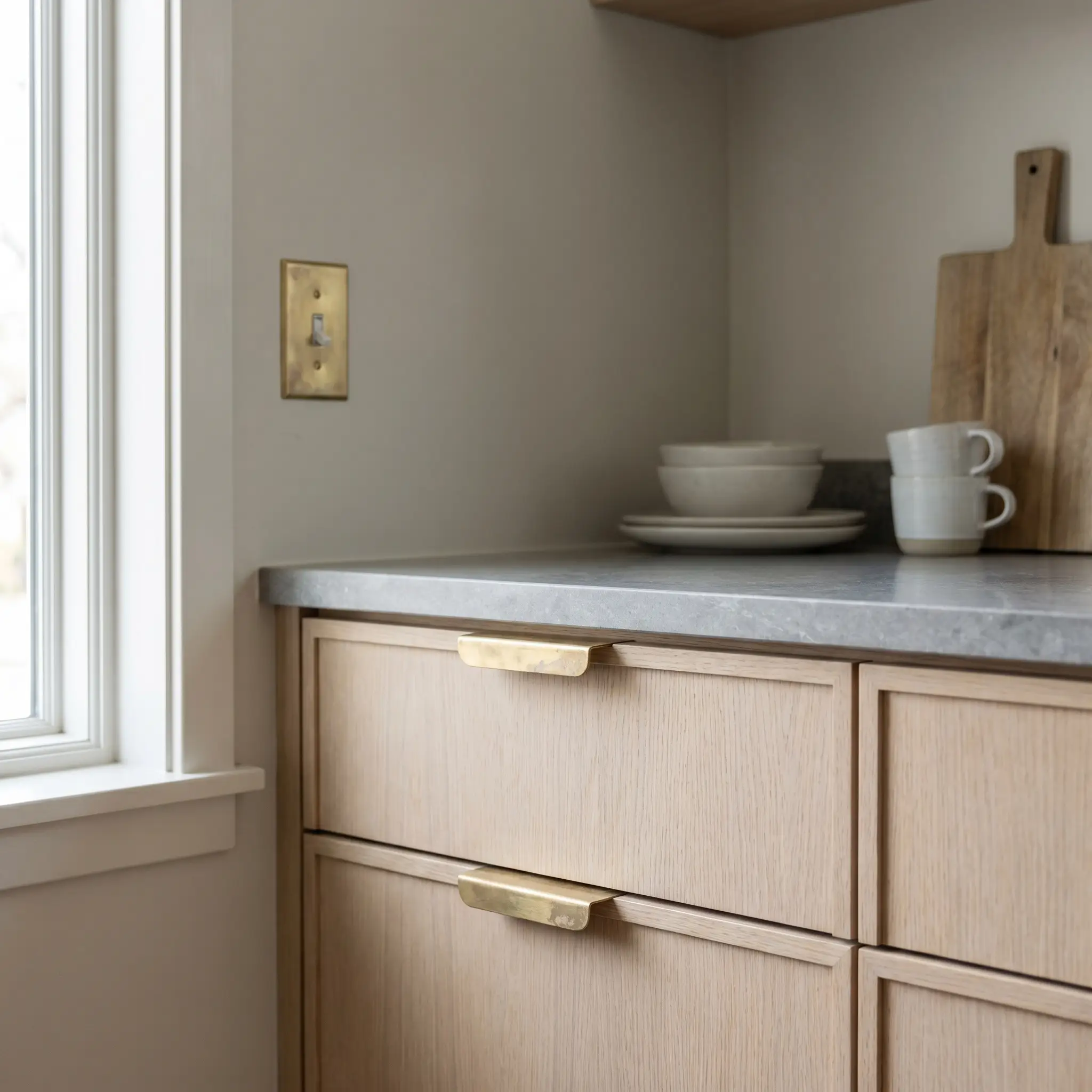 Raw, unlacquered brass edge pulls on pale rift-sawn oak cabinetry bring an evolving wabi-sabi patina to Japandi style kitchens.