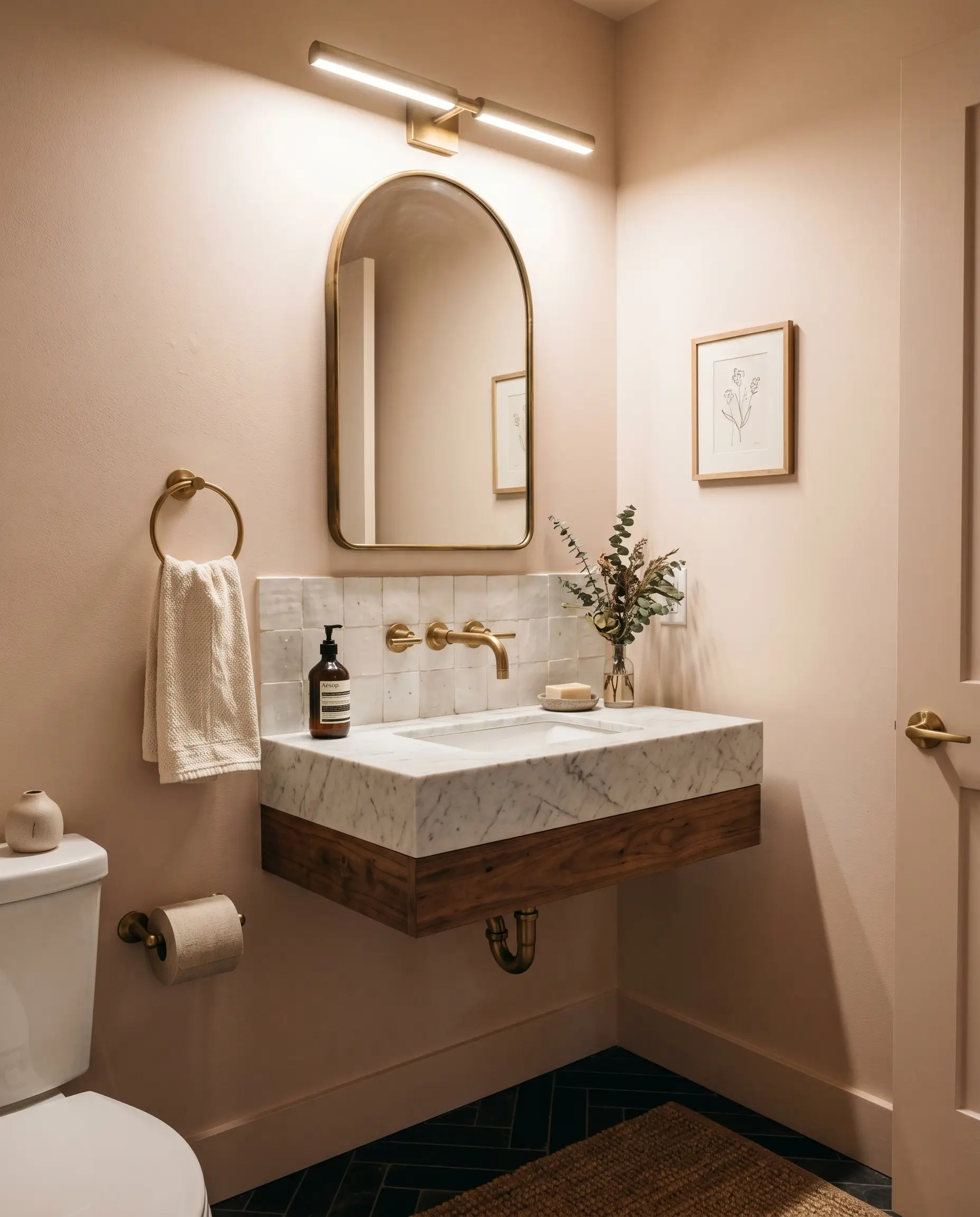 An unlacquered brass wall-mounted faucet and honed marble sink sit beneath luminescent tint walls and a handmade white zellige tile backsplash in a tiny powder room.