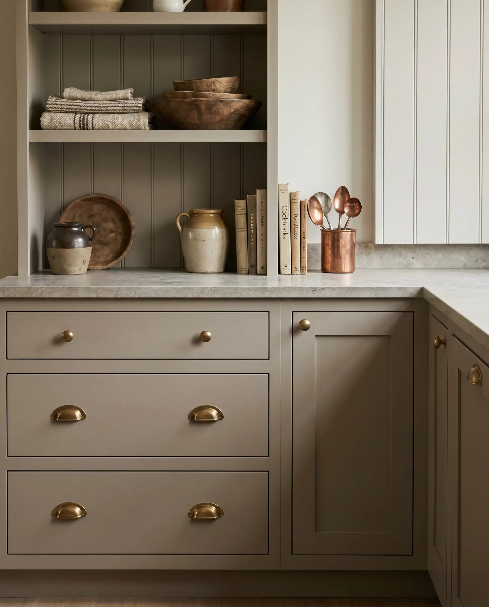 Unlacquered brass cup pulls and ball knobs add a living patina to warm greige kitchen cabinetry, set above a honed stone counter.