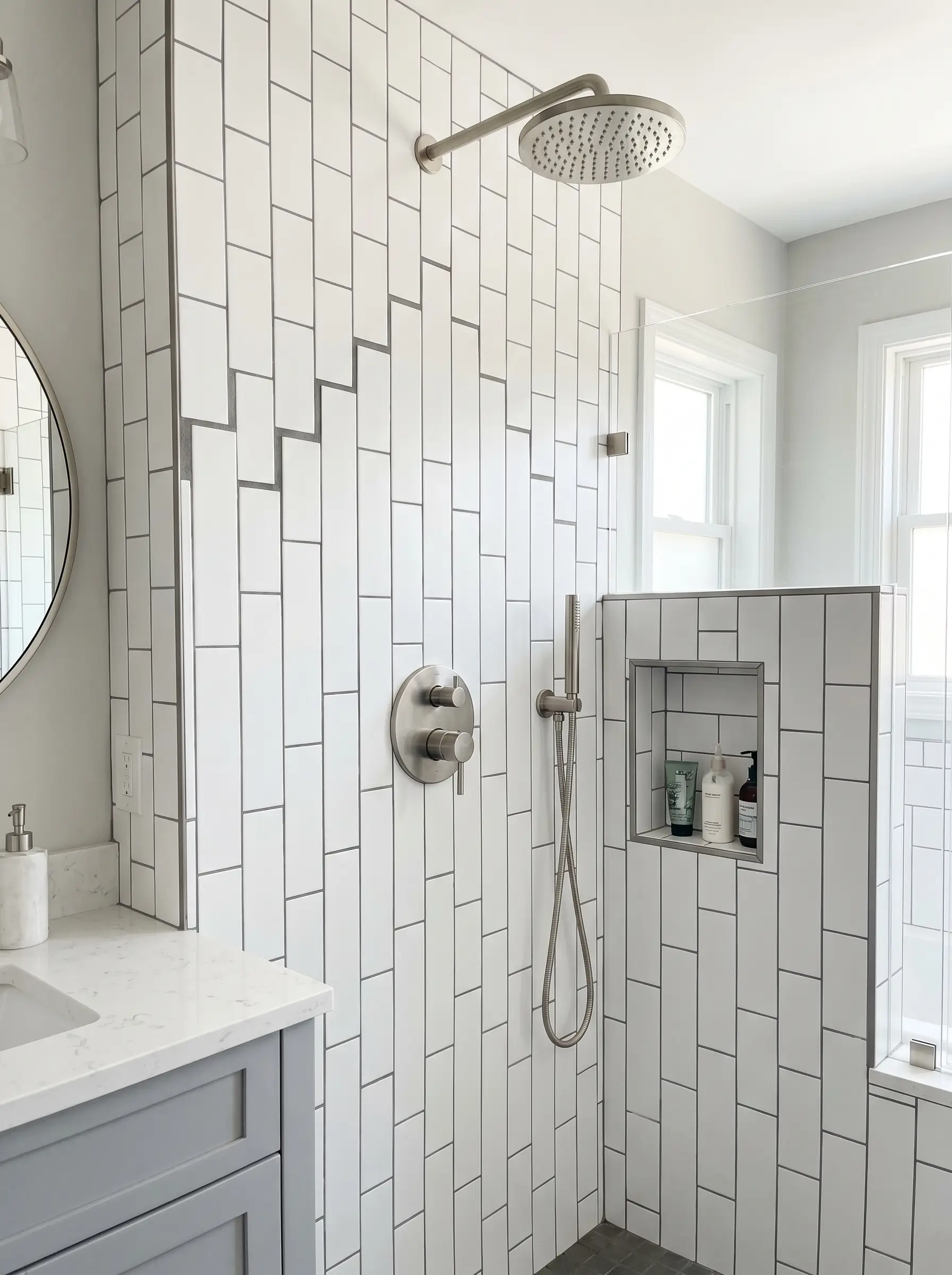 A subway tile bathroom shower wall features a vertical offset half-drop layout with dark gray grout joints, brushed nickel hardware, and glass enclosure.
