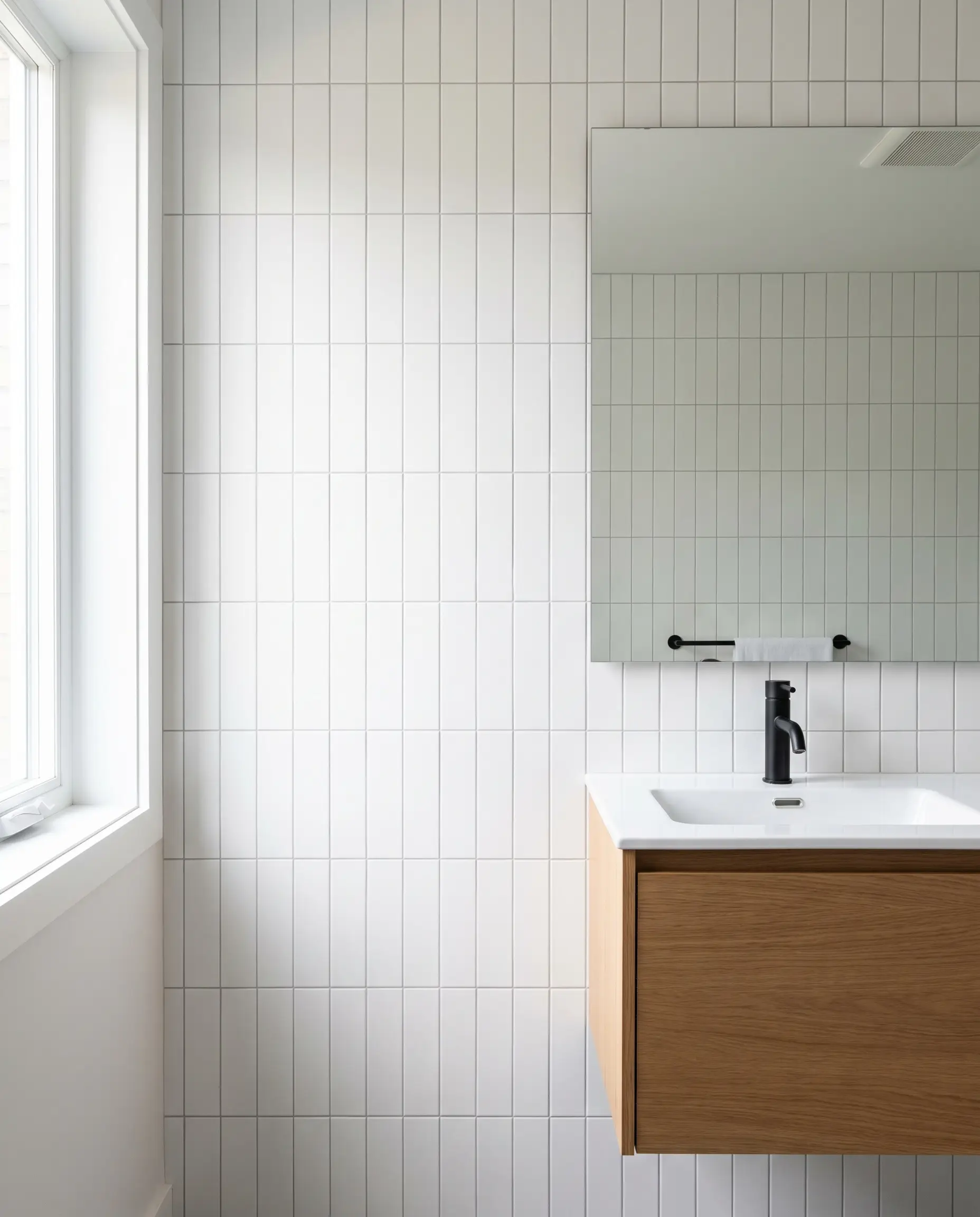 Flat white ceramic tiles in a vertical straight stack layout cover the vanity wall behind a sleek floating oak cabinet and frameless mirror.