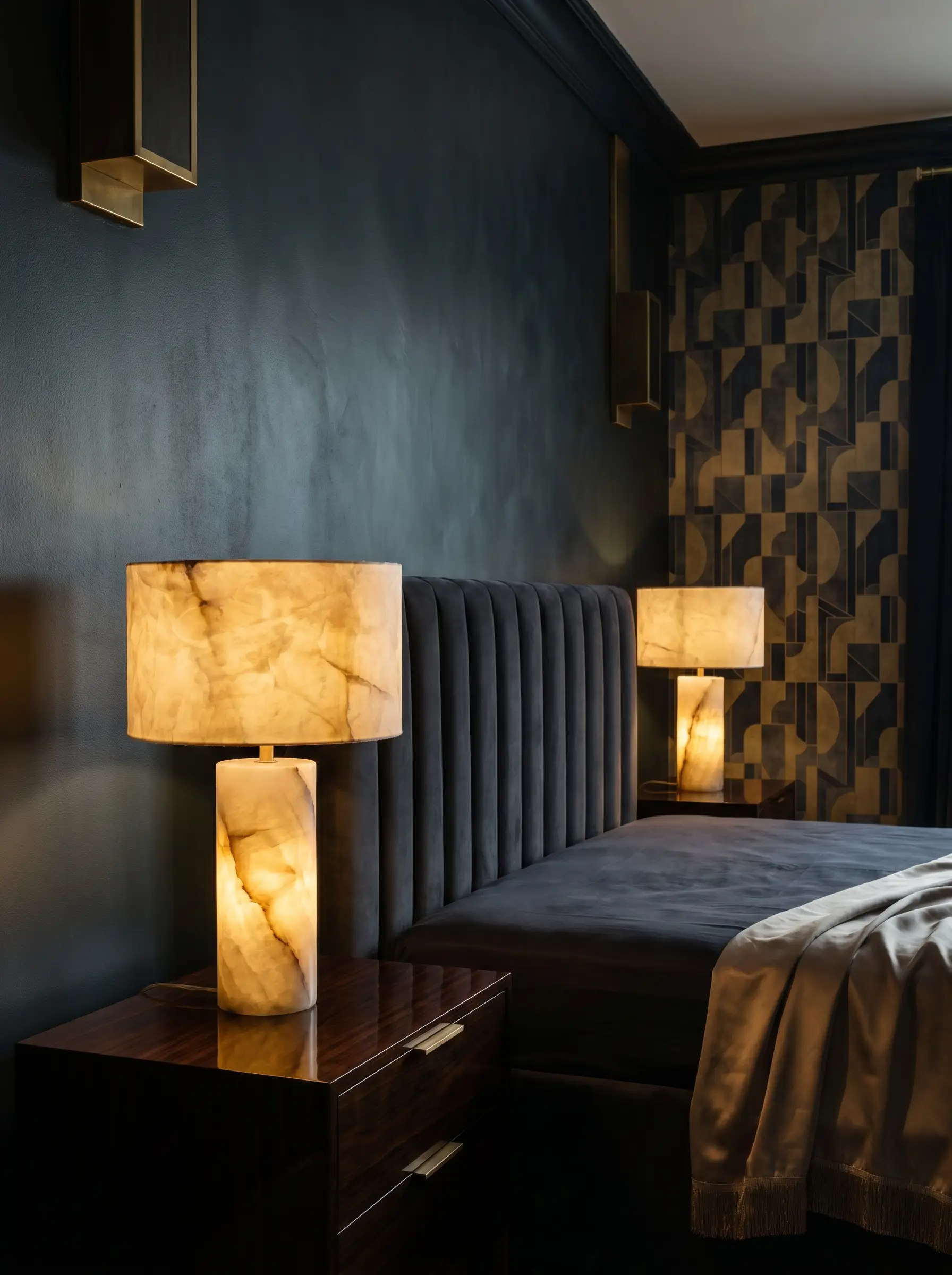 Heavy veined solid alabaster stone bedside lamps rest on dark polished nightstands next to a plush channel-tufted bed against a moody painted wall.