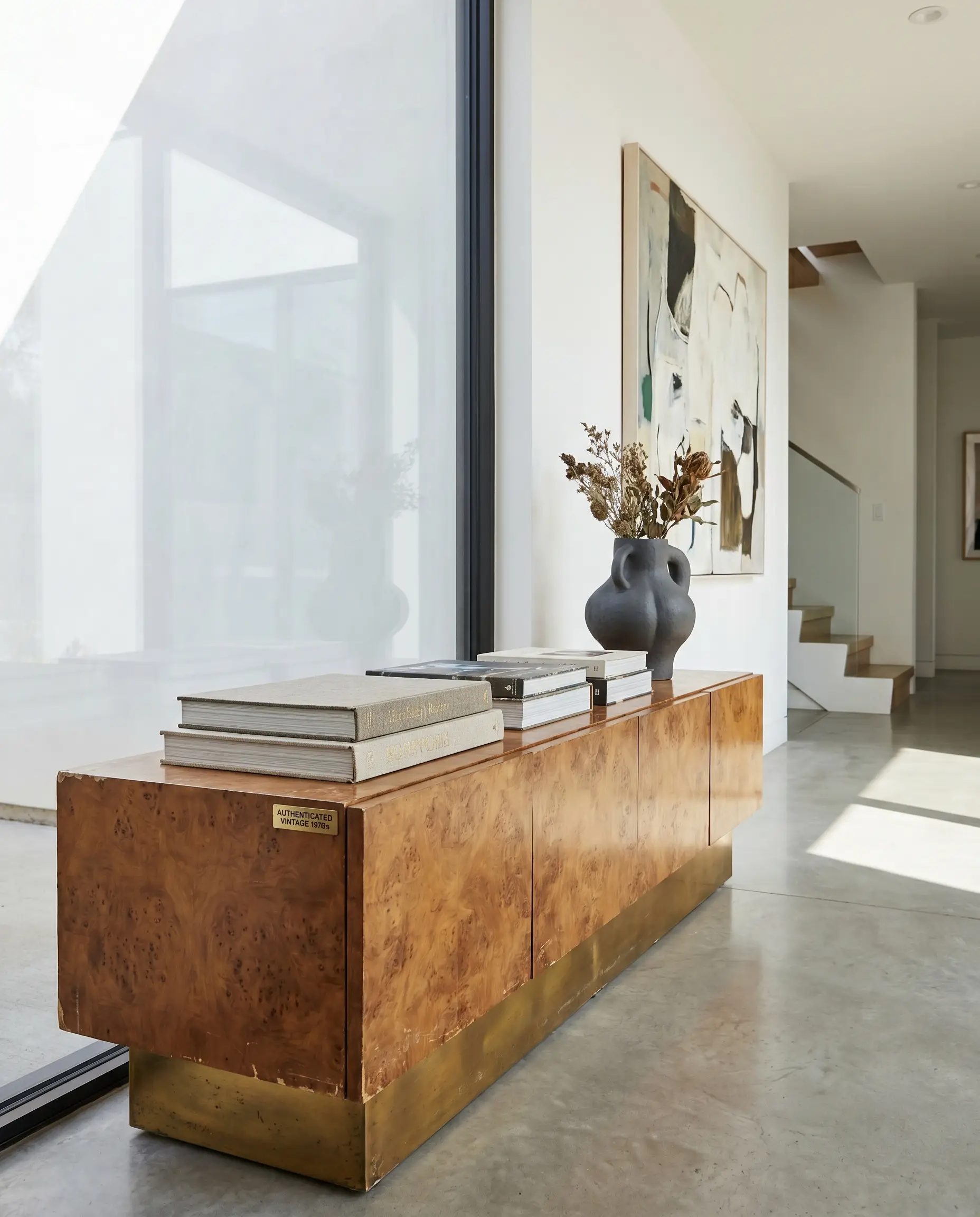 An authenticated vintage 1970s Milo Baughman-style burl wood console table displays high-end art books and a structural vase against crisp contemporary foyer walls.