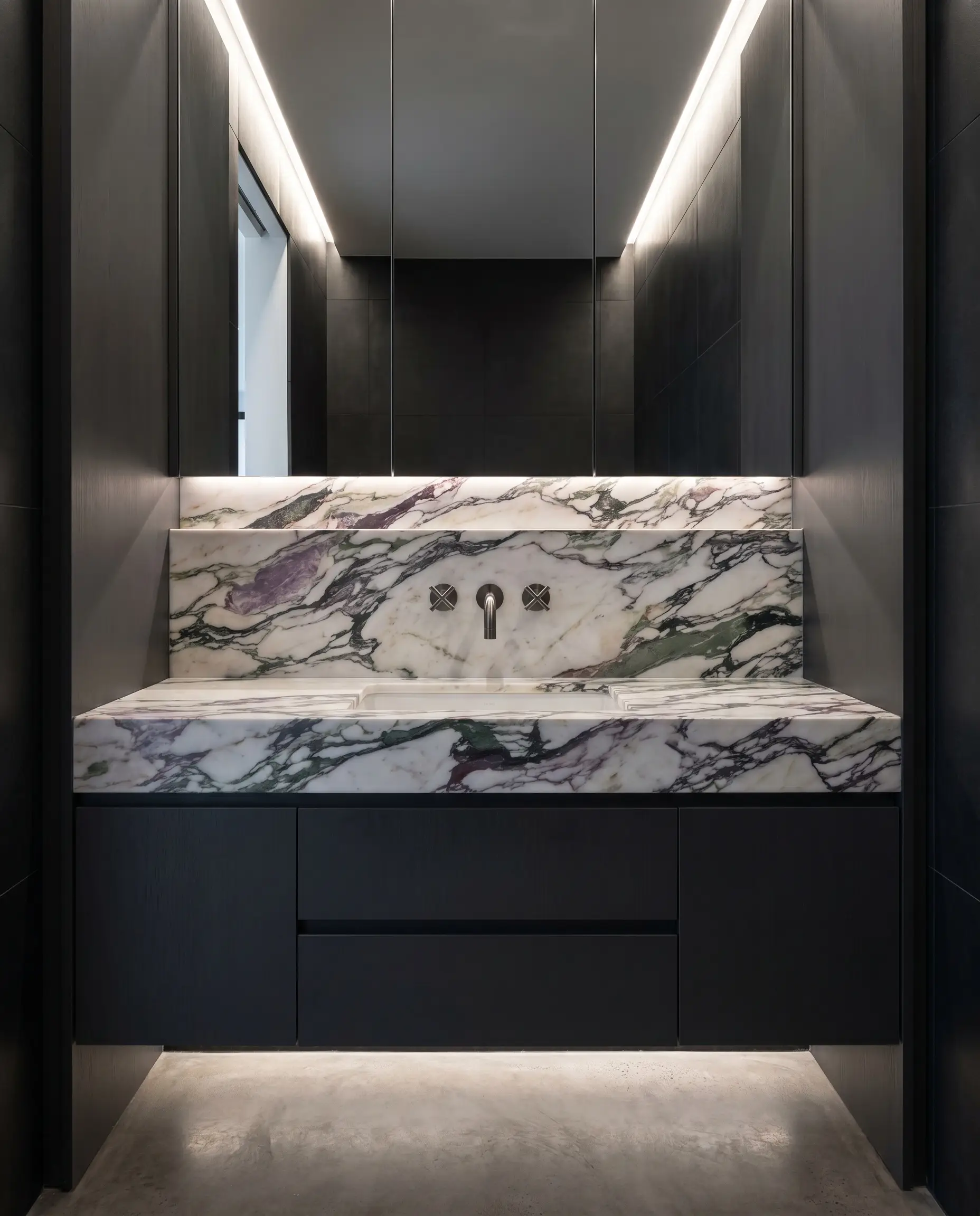A brushed gunmetal faucet is wall-mounted directly through a vibrant calacatta monet marble powder room vanity splashback surrounded by matte charcoal millwork.