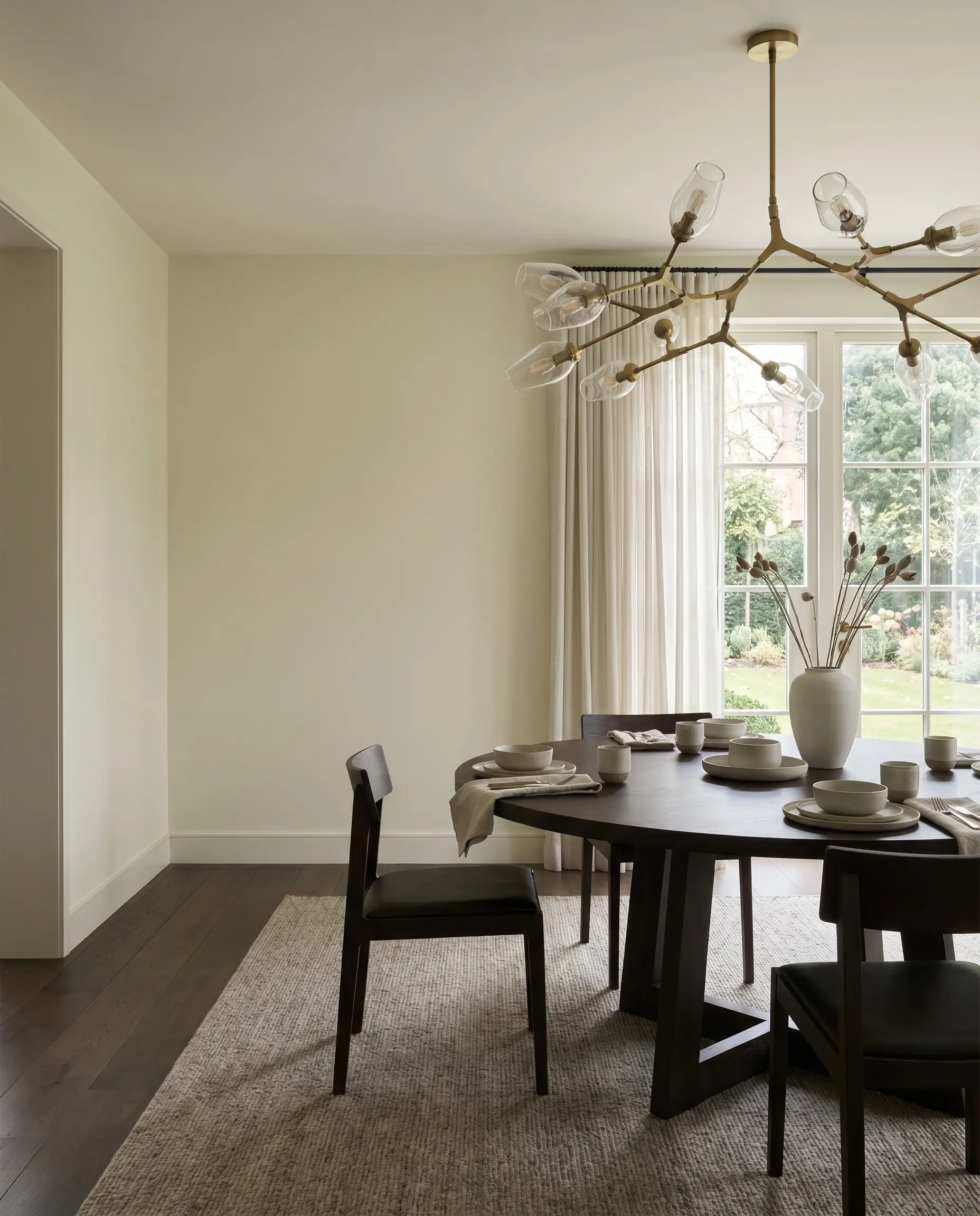 A modern sculptural chandelier hangs above a refined dining area featuring Benjamin Moore White Dove ivory matte walls and legacy red oak flooring.