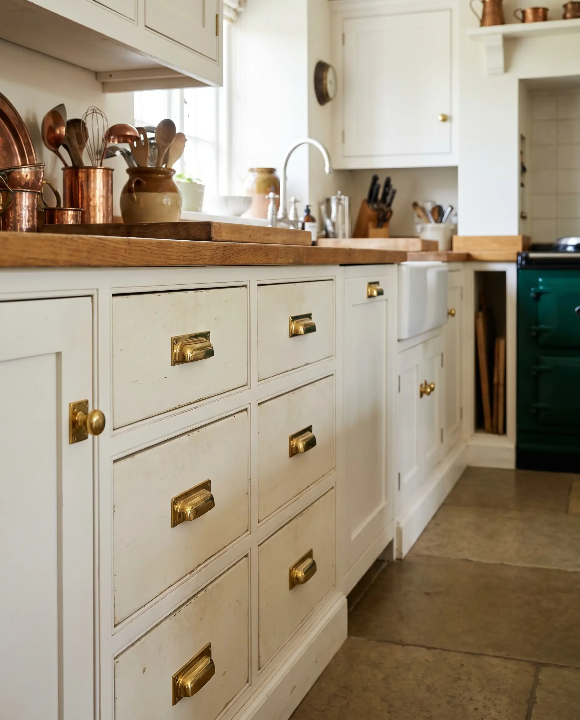 Solid brass pulls and matching rectangular backplates align perfectly on the wood stiles of pristine white doors in a bespoke heritage English kitchen.