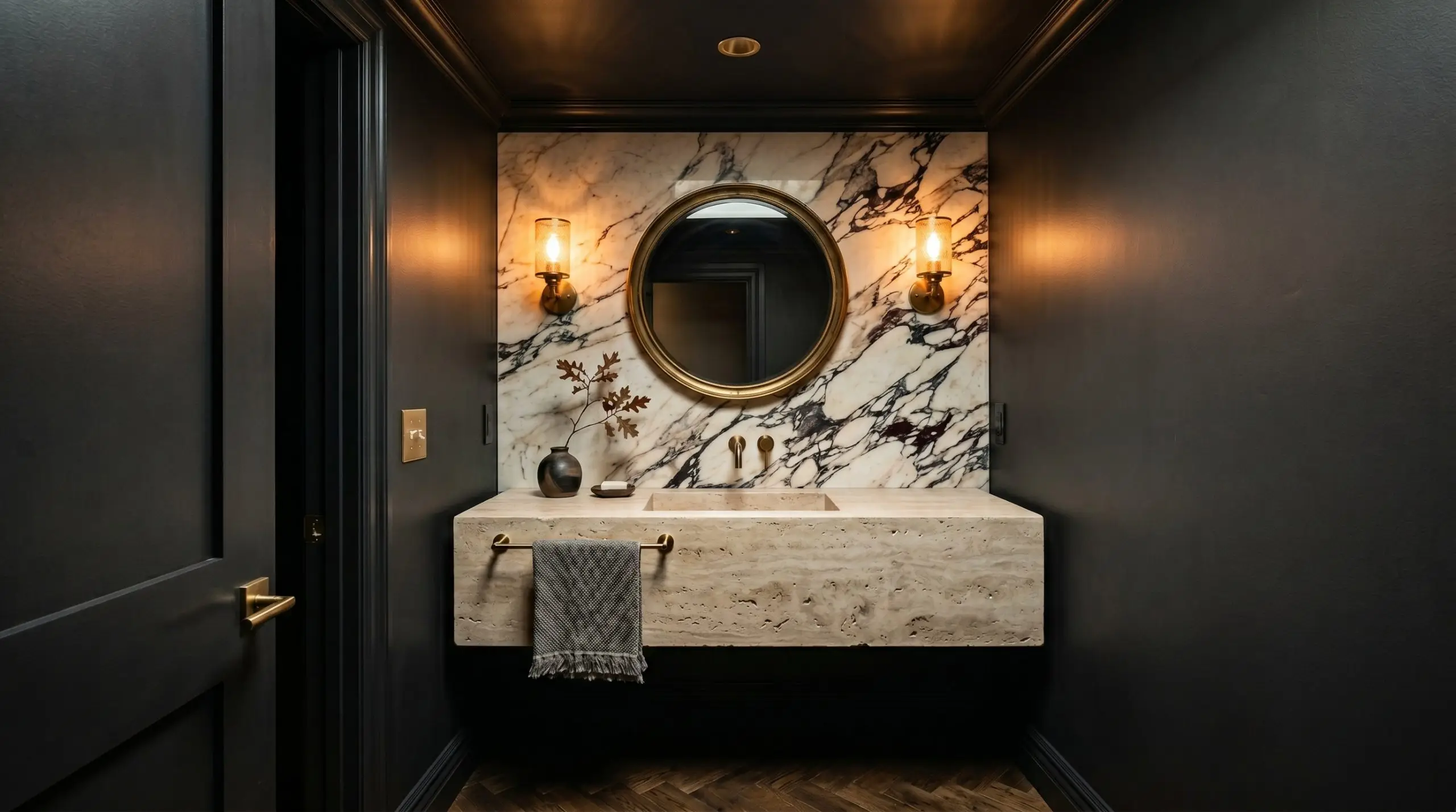 A windowless powder room is completely color-drenched in Benjamin Moore Onyx (Hex #353434), featuring glowing brass sconces, a floating travertine vanity, and a marble backsplash.