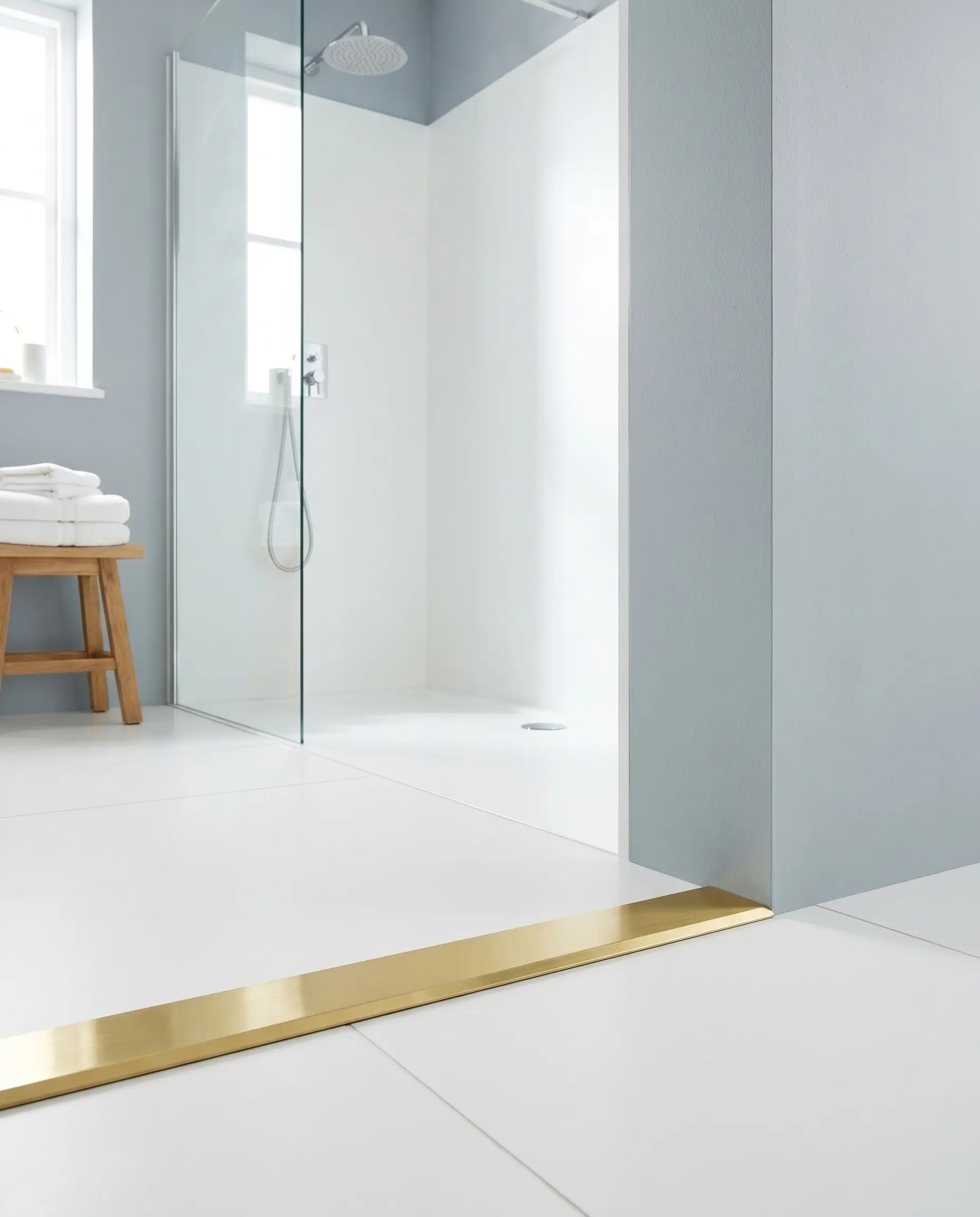 A crisp brass metal edge profile seamlessly caps large-format white porcelain tiles at the entry of a minimalist wet room.