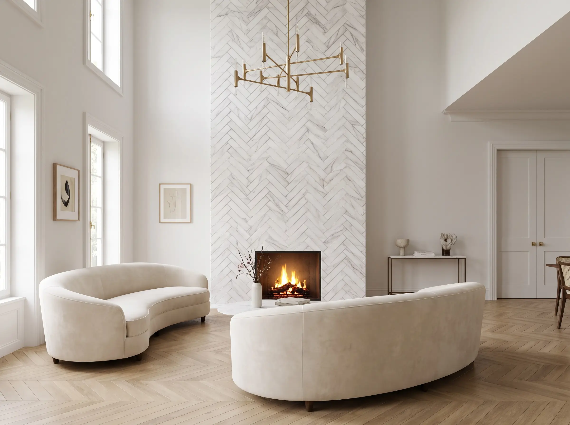 A sweeping floor-to-ceiling herringbone fireplace surround clad in elongated Calacatta marble tiles anchors a Parisian chic living room with a curved sofa and brass chandelier.