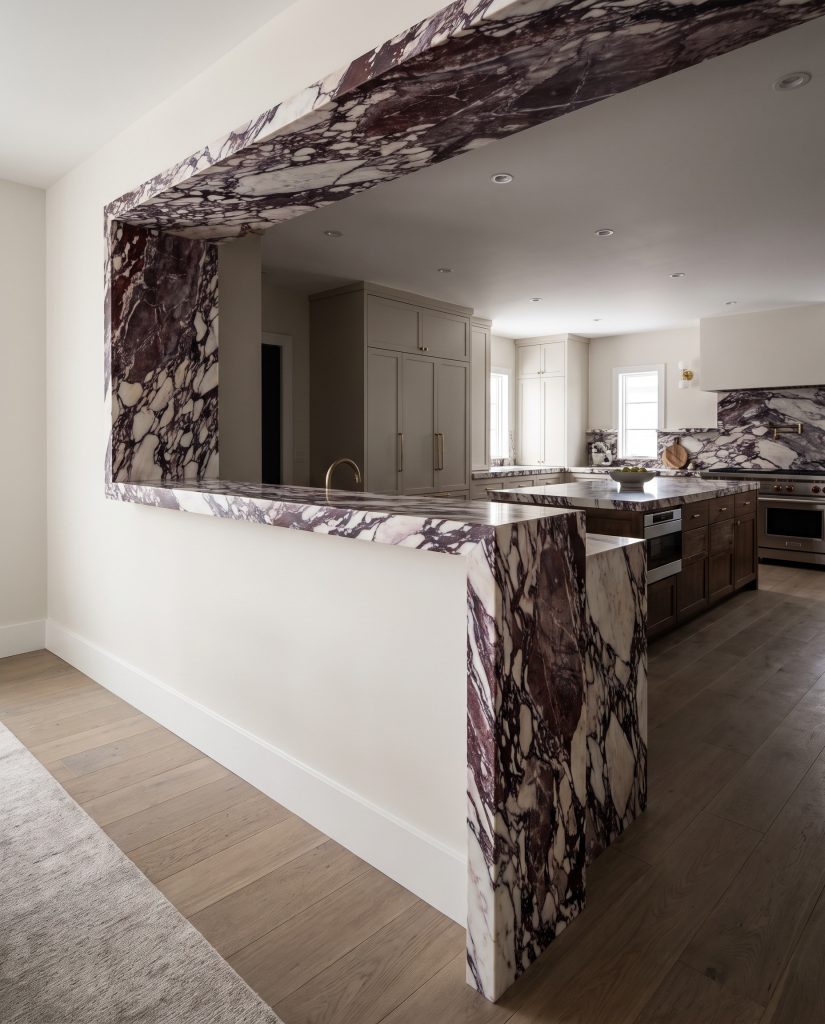 A dramatic Calacatta Viola marble slab cascades down a kitchen partition in a seamless mitered waterfall edge against Sherwin-Williams Alabaster painted walls.