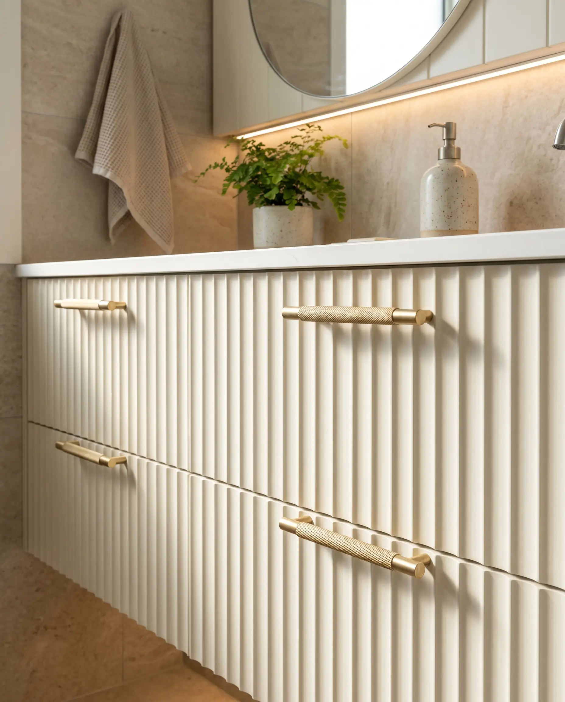 Solid brass knurled bar pulls mounted on a Chantilly Lace fluted vanity within a modern white and gold bathroom setting.