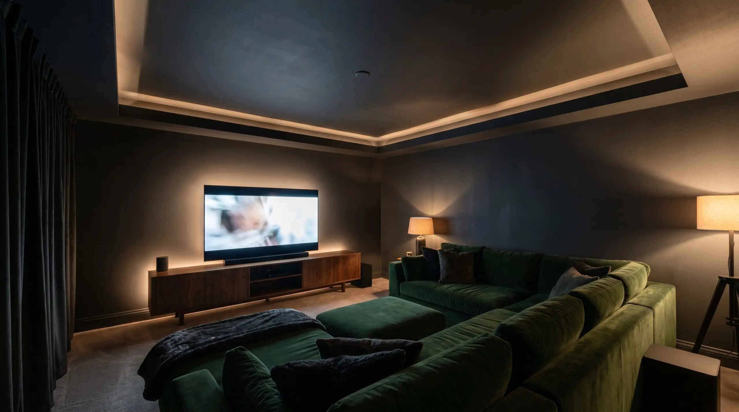A plush velvet sectional and a warm wood media console anchor a dark media room featuring a soft black-charcoal color-drenched ceiling.