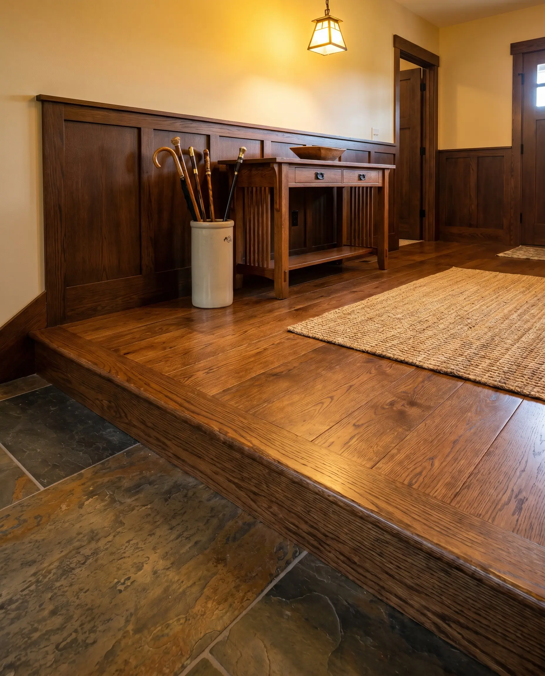 A custom-milled wood reducer perfectly color-matched to site-finished solid hardwood sits flush against a higher natural stone tile floor in a traditional craftsman entryway.
