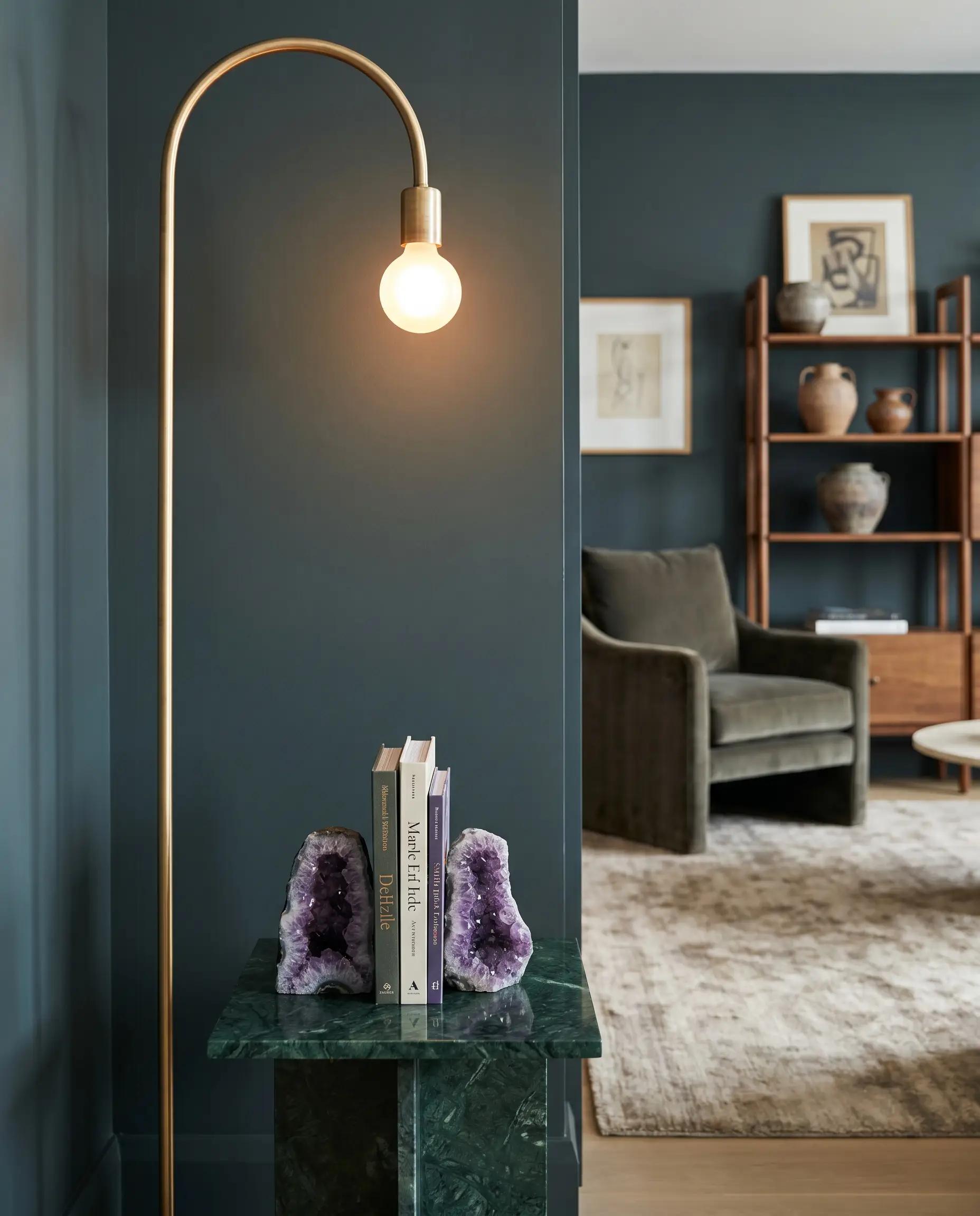 A deep green marble side table displays violet amethyst geodes beside an unlacquered brass floor lamp against Benjamin Moore Regent Green walls, perfecting Feng Shui home decorating.