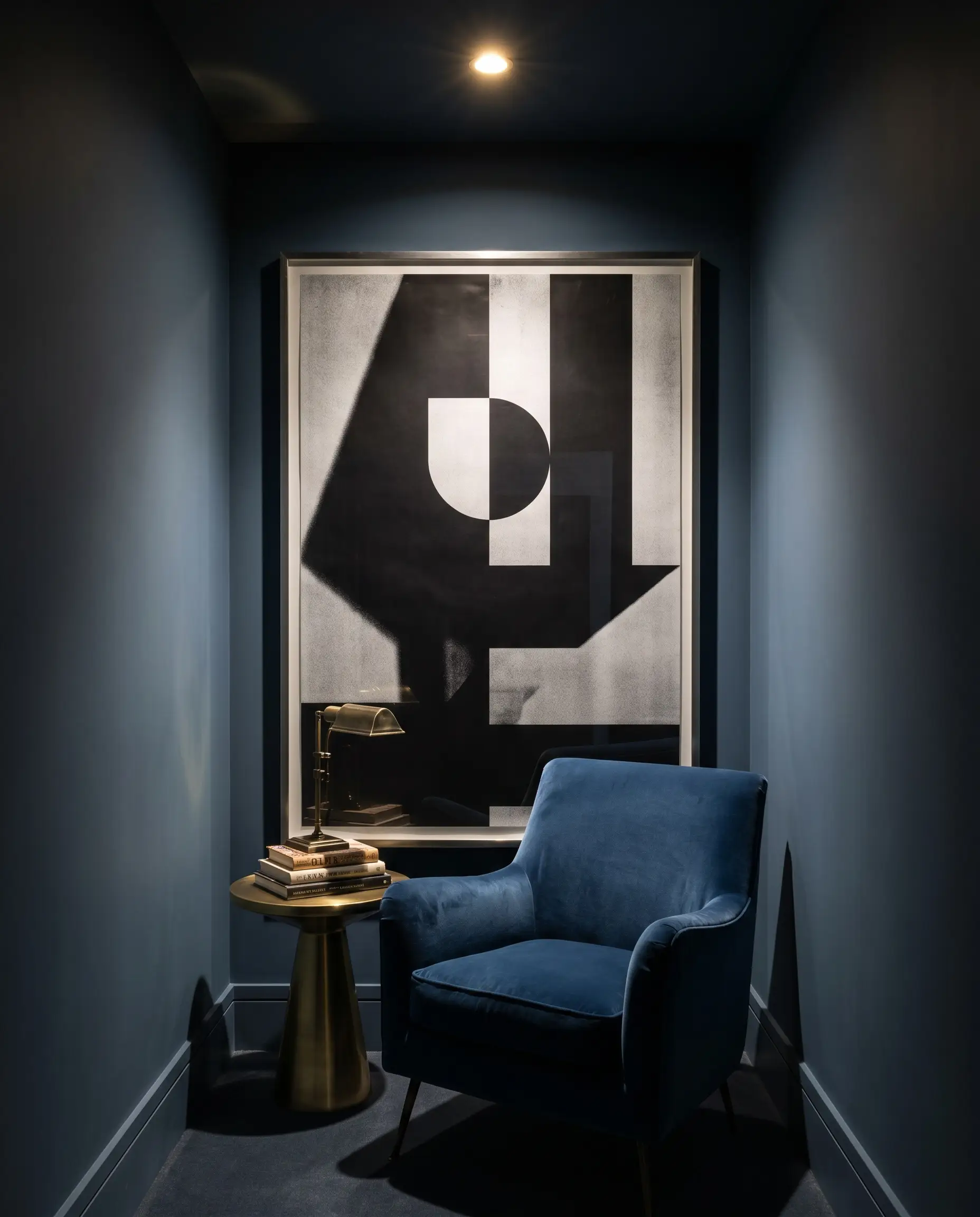 A massive high-contrast graphic poster in a thin metal frame dominates a Hague Blue painted jewel box nook featuring a velvet armchair.