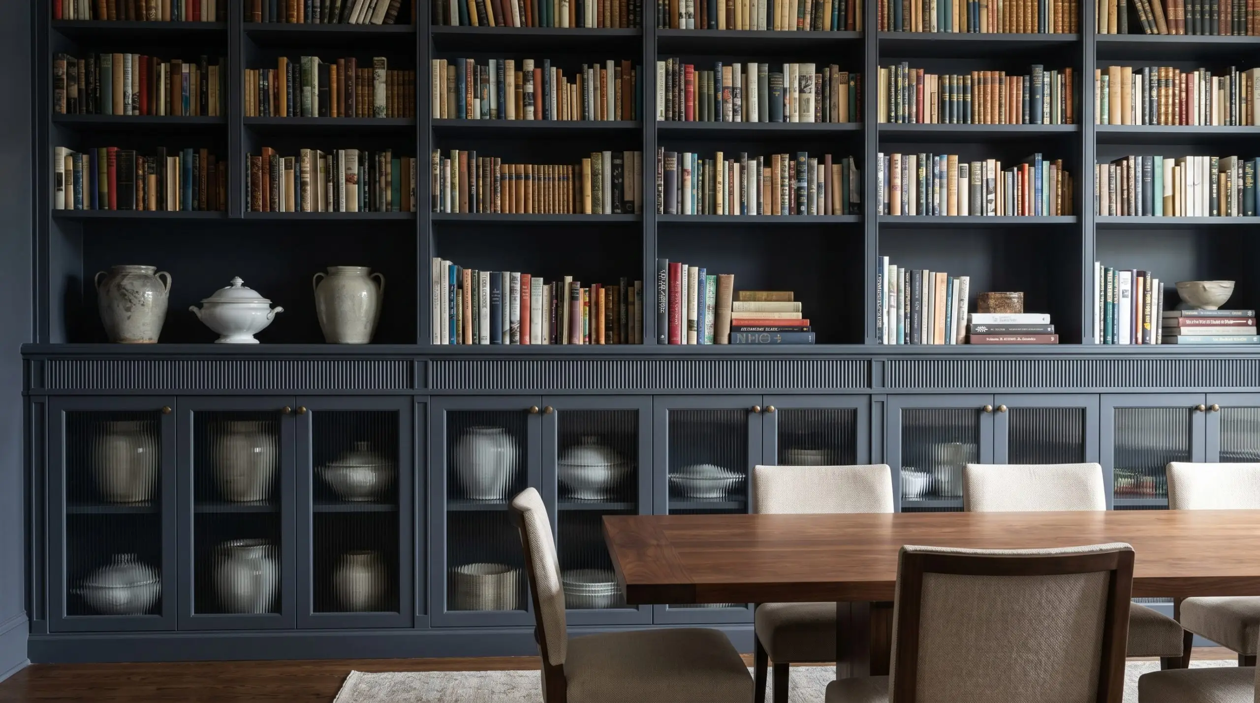 A dual-purpose mini library design features fluted fascia trim and Benjamin Moore Hale Navy base cabinets with reeded glass doors behind a dining table.