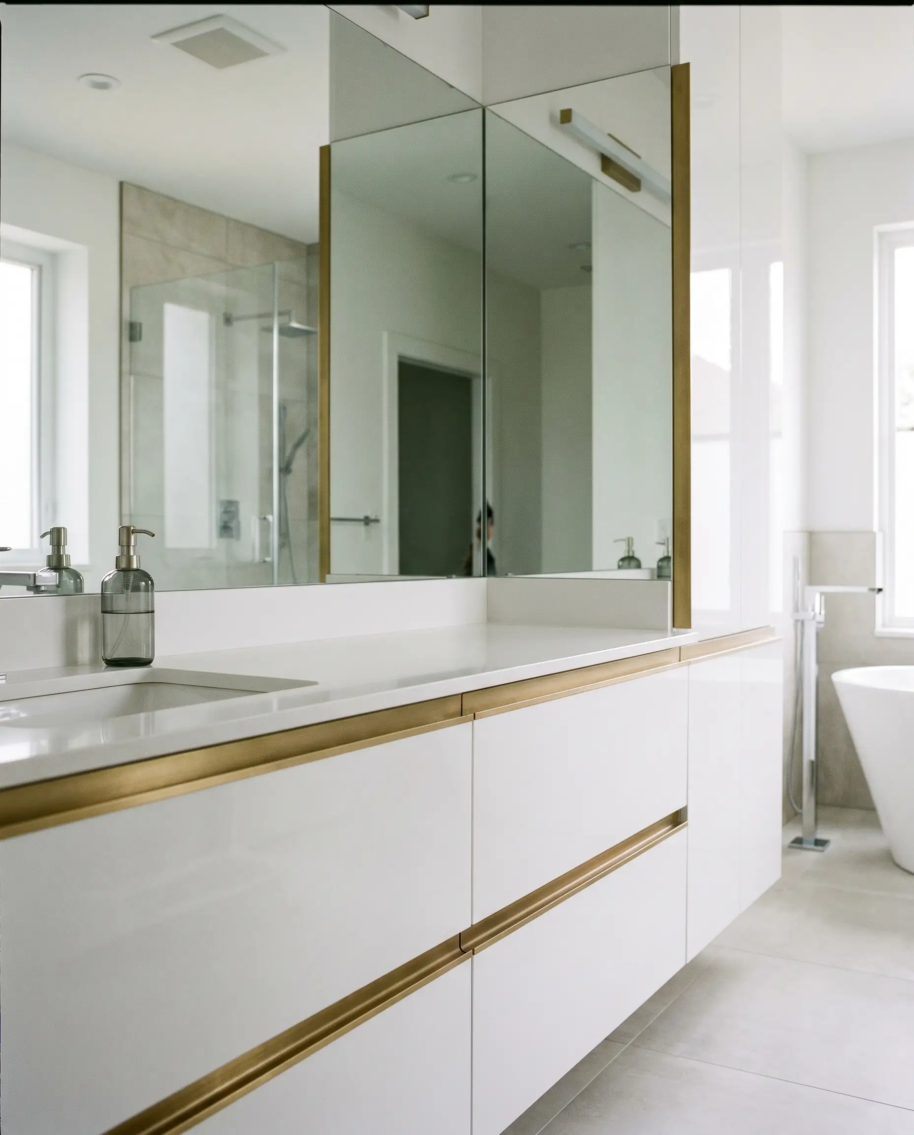 Flat brushed brass continuous finger-pull hardware edges sleek high-gloss white polyurethane cabinetry below a minimalist white basin.