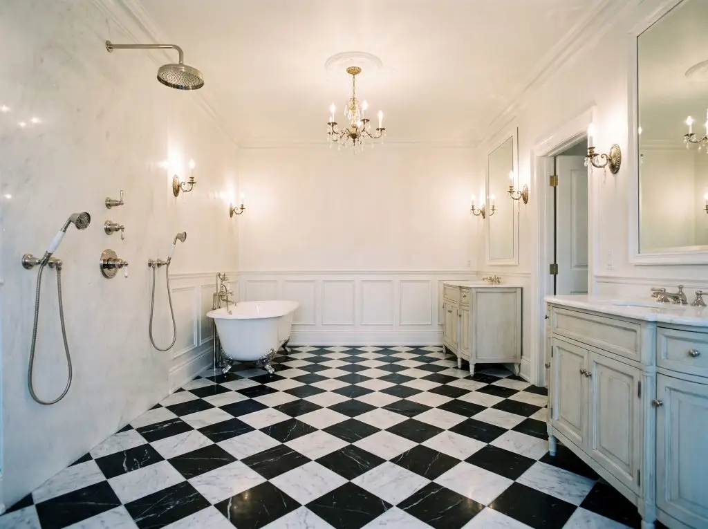 A honed marble checkerboard floor of Matte Carrara and Nero Marquina tiles extends seamlessly toward a freestanding clawfoot tub and crisp white wainscoting.