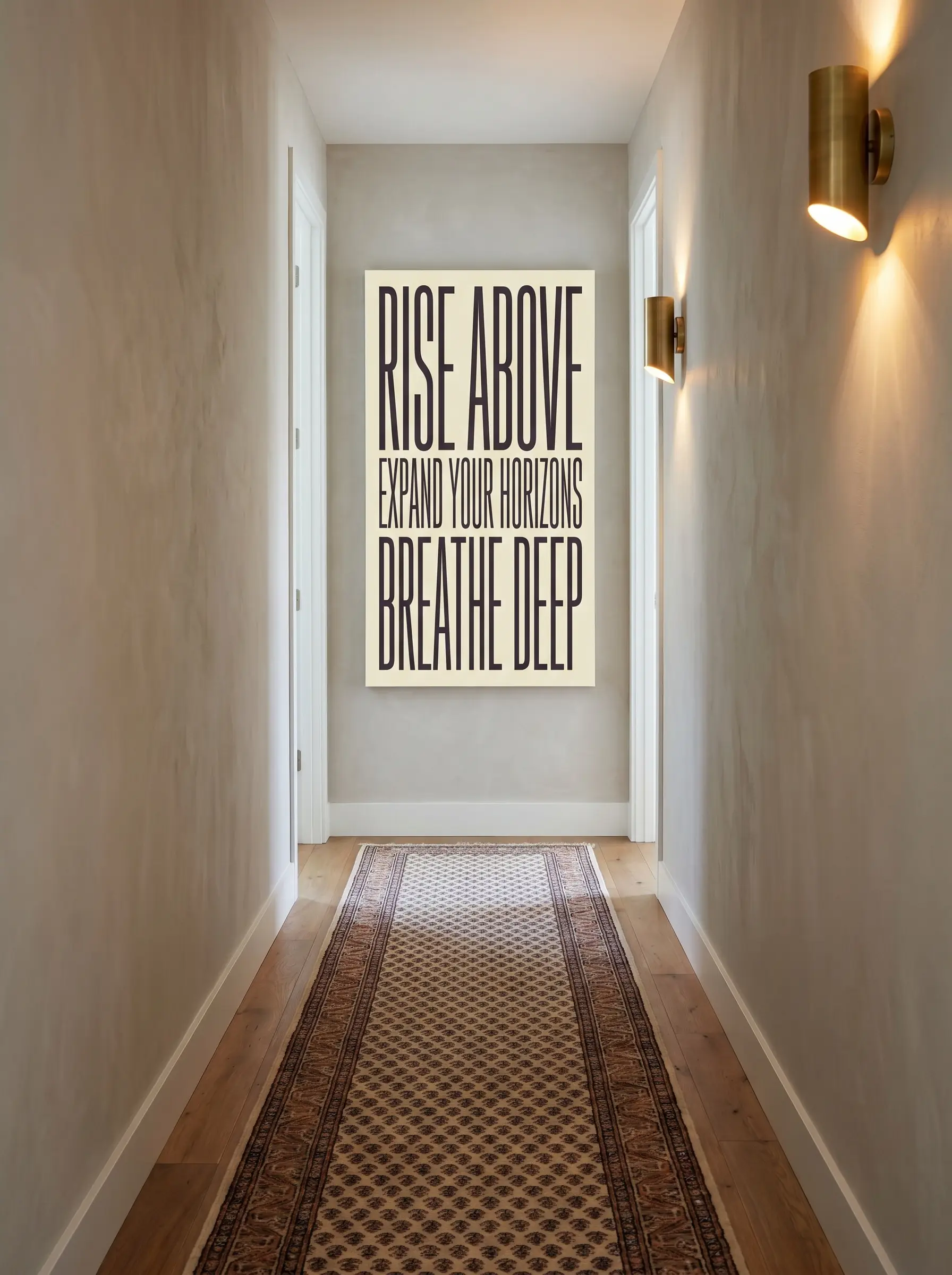 A tall panoramic vertical typographic poster hangs exactly at eye level at the end of a narrow hallway transition above a patterned runner rug.