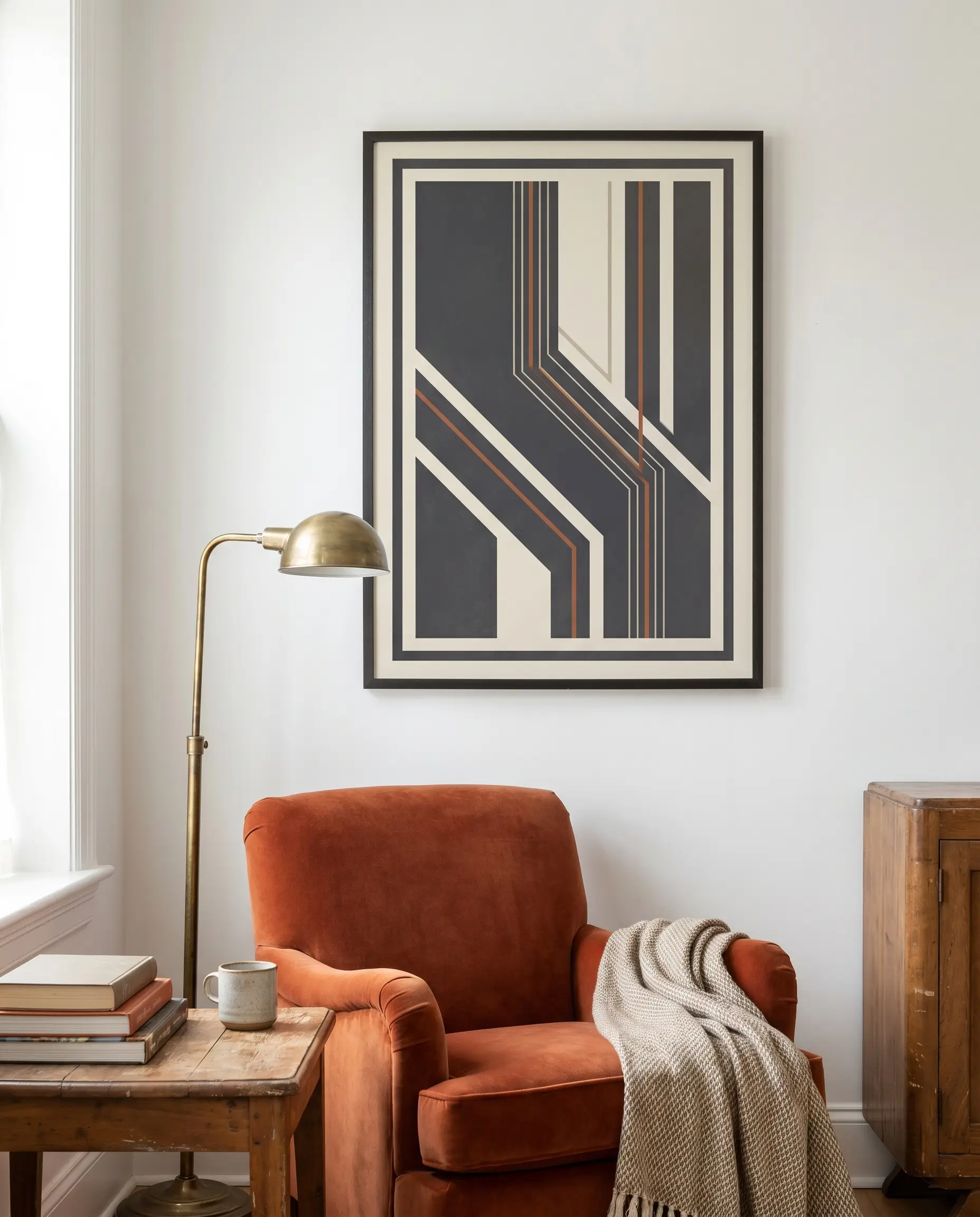 A framed graphic poster featuring a rust-orange accent hue hangs beside a sumptuous rust-orange velvet accent chair and a brass floor lamp.
