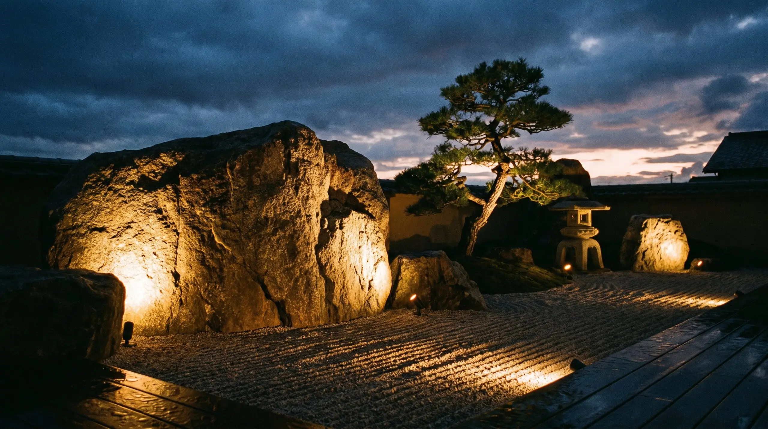 Directional low-voltage LED uplights graze the rough faces of massive anchor boulders, casting long shadows across a meticulously raked gravel bed.