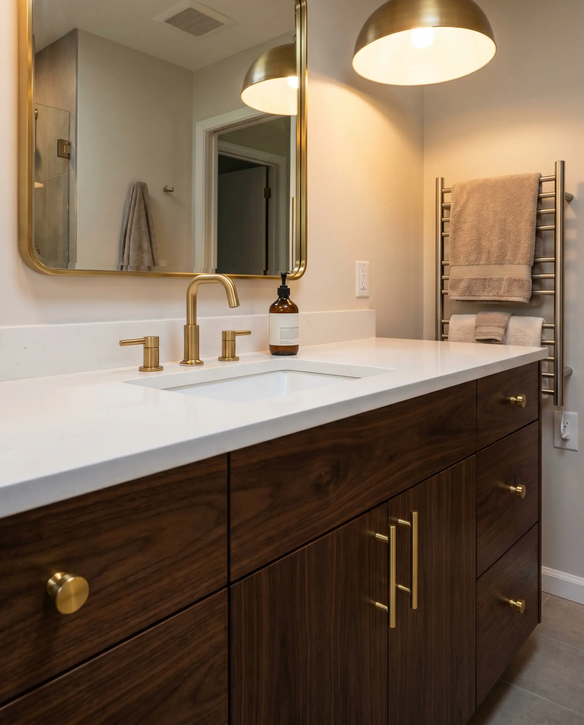 Brushed gold cylinder knobs shine brilliantly against the heavy dark grain of a flat-panel natural walnut vanity below a crisp white quartz countertop.