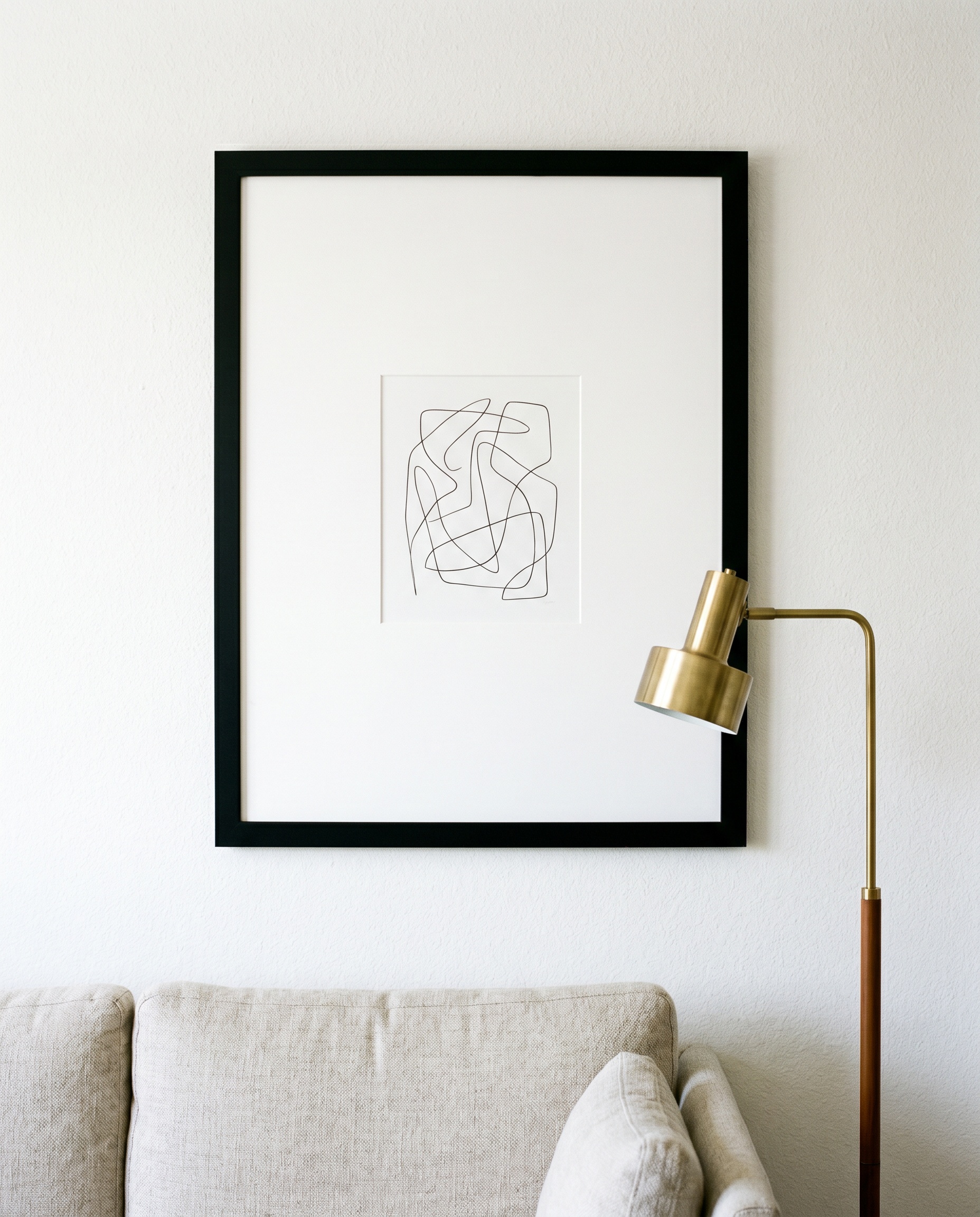 Interior decorating using posters incorporates a modest graphic print housed in a massive black frame with an oversized passe-partout above a cozy fabric sofa.