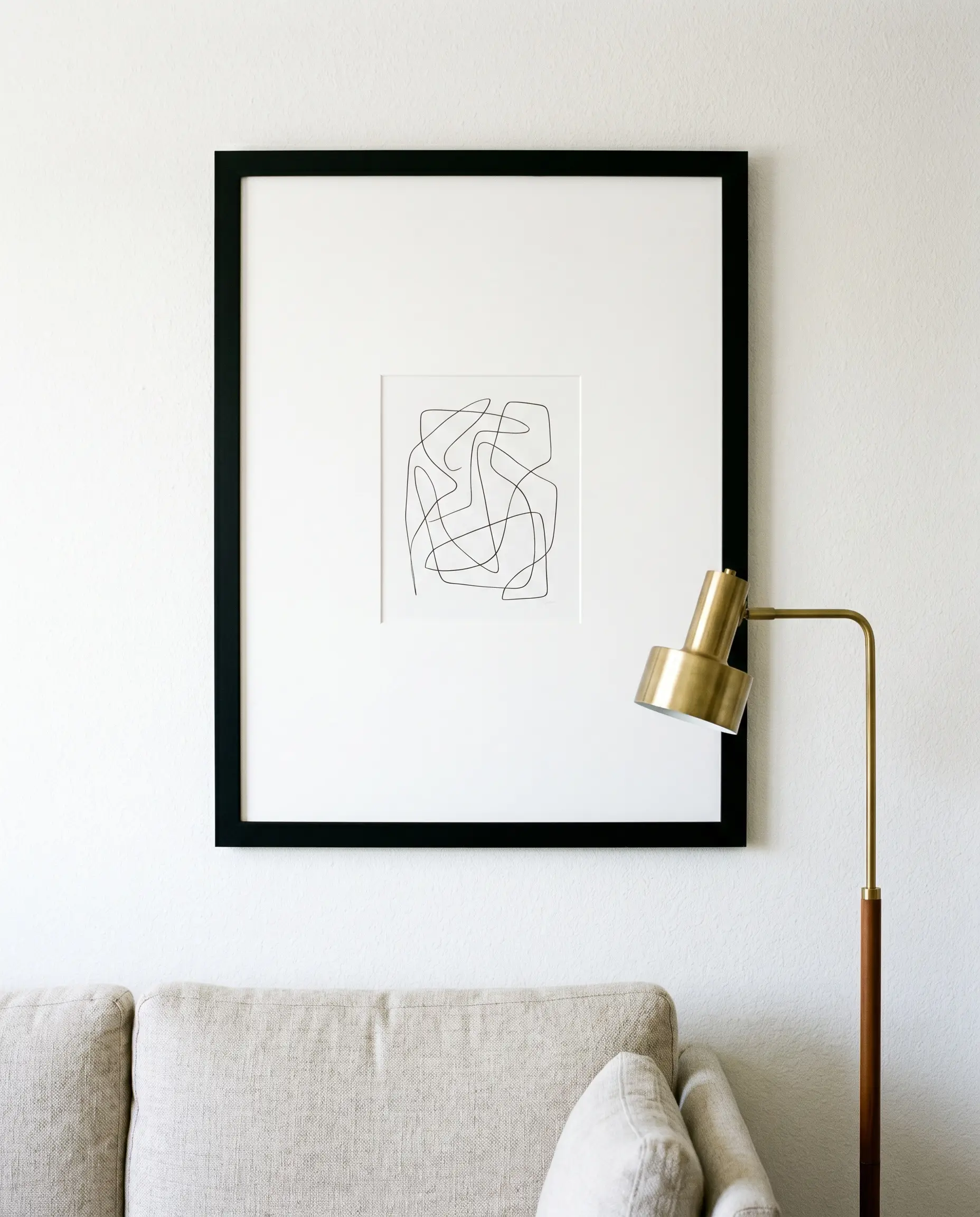 Interior decorating using posters incorporates a modest graphic print housed in a massive black frame with an oversized passe-partout above a cozy fabric sofa.