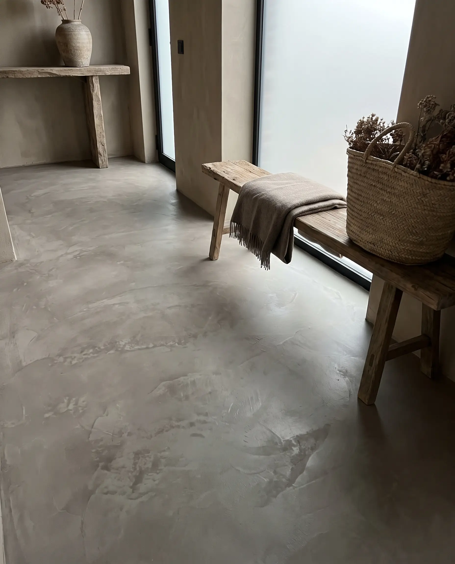 Hand-troweled poured microcement grounds an organic wabi-sabi entryway featuring a raw wood bench and woven basket.