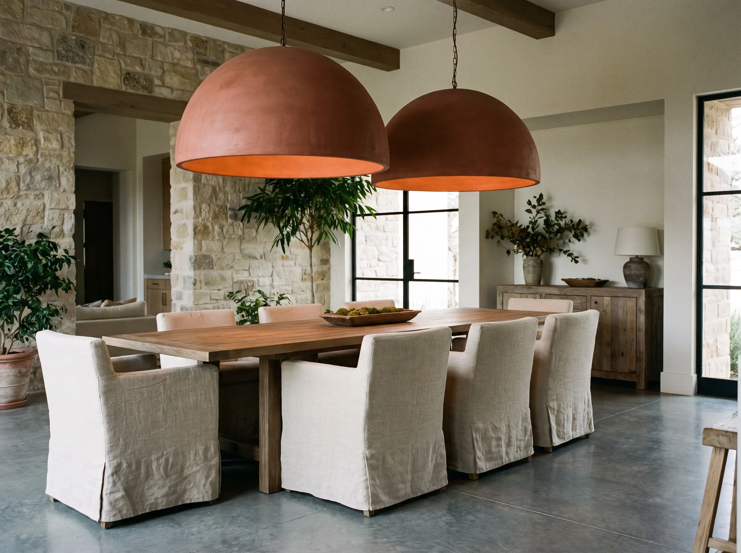 Large raw terracotta dome pendants hang low over a warm wood dining table and cozy linen dining chairs in a Mediterranean modern room.