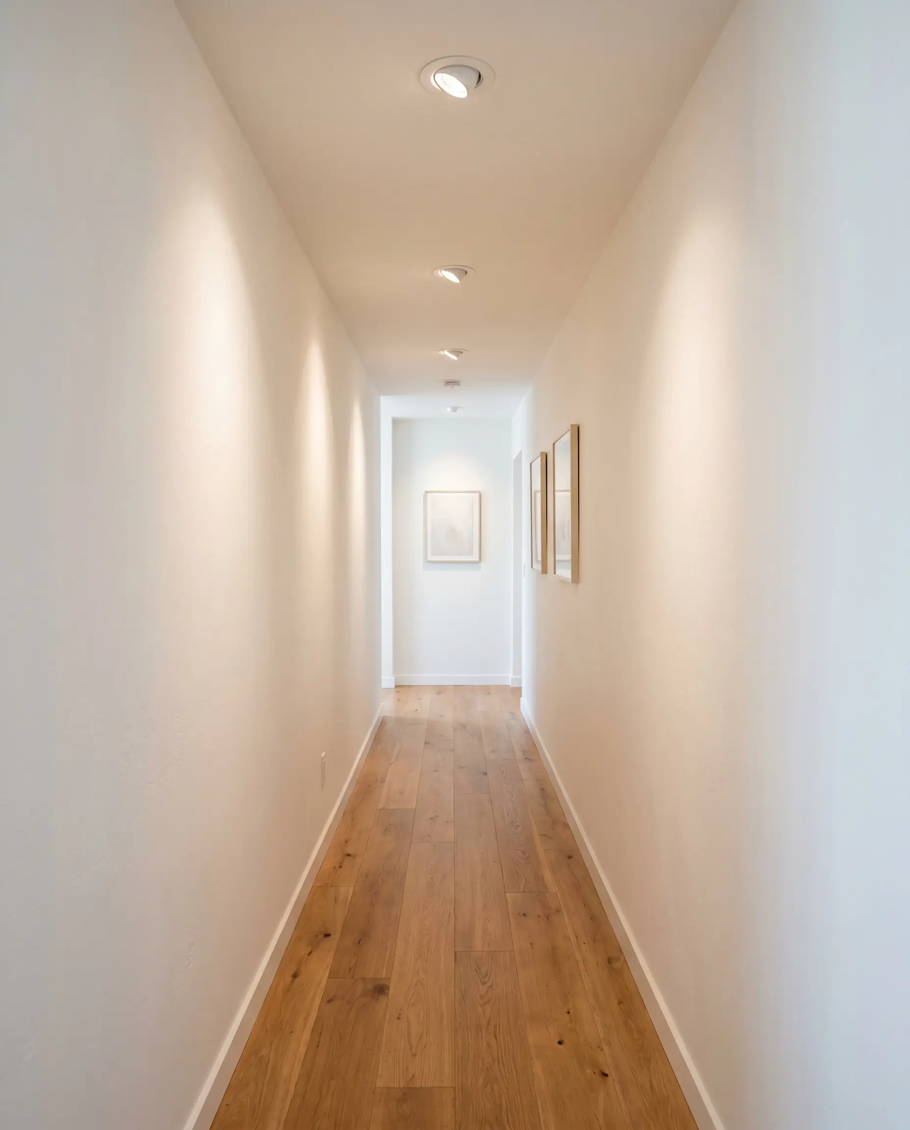 Three-inch LED recessed ceiling lights with gimbal trims wash subtle texture over matte white walls to create expansive narrow hallway wall decor.