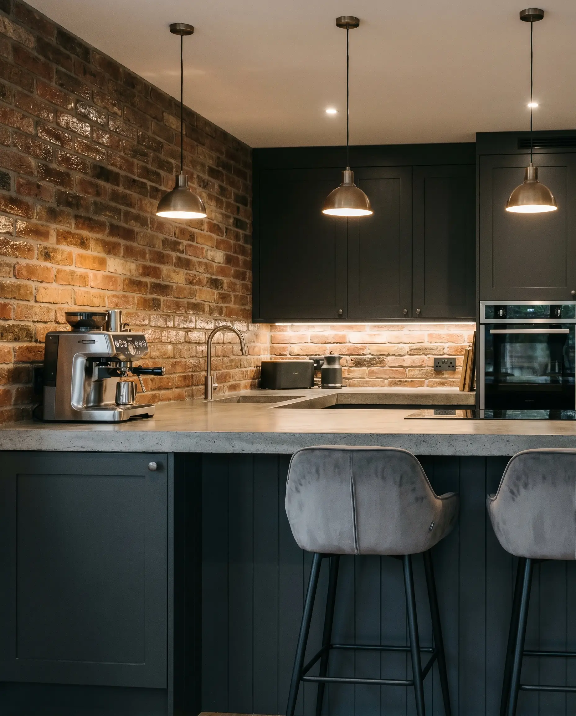 Raw unglazed brick slips form a textured kitchen backsplash tile meeting a poured concrete countertop and moody Sherwin-Williams Iron Ore painted cabinetry.