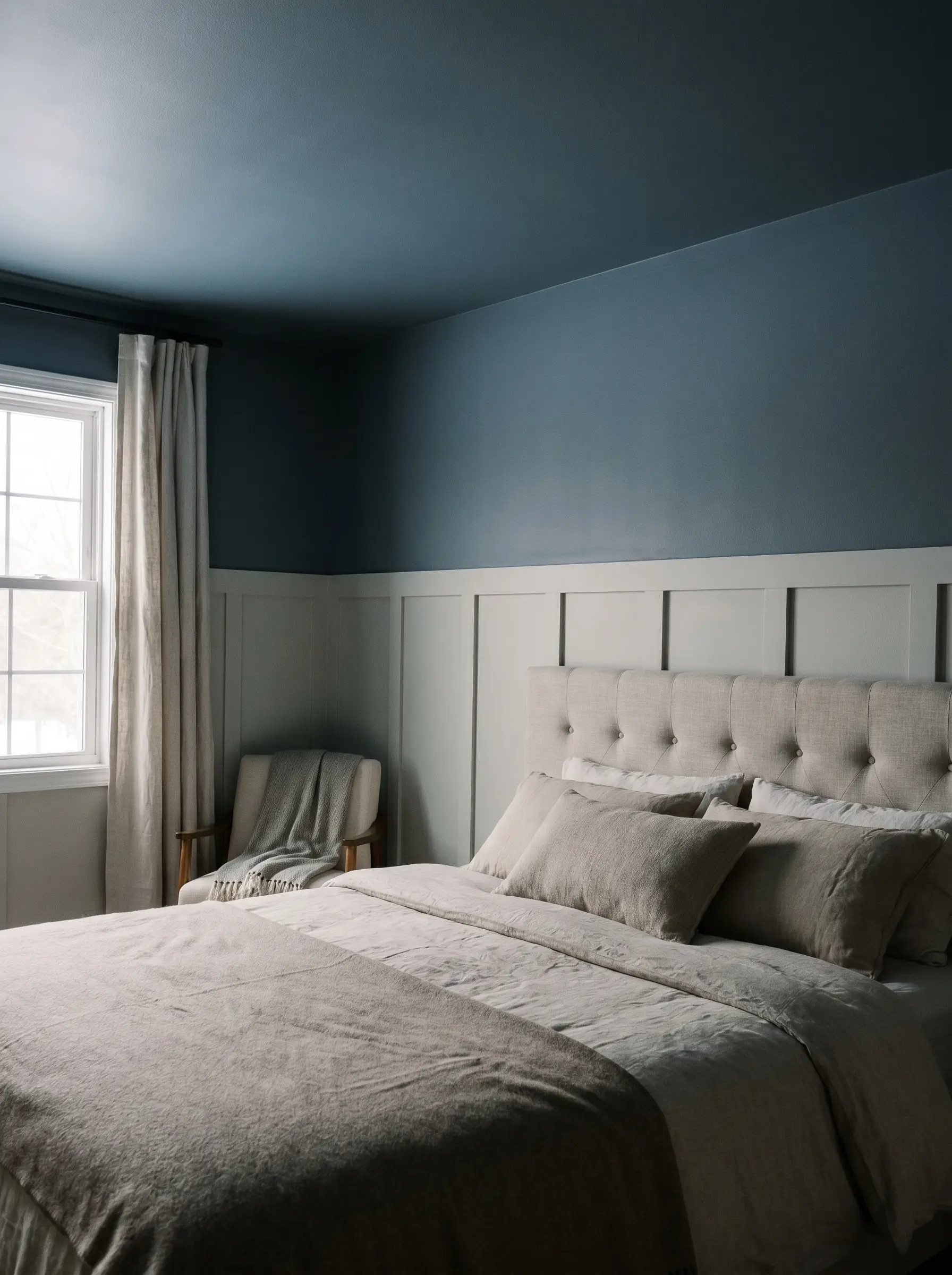 A tufted headboard rests against warm silver lower wainscoting that transitions into slate blue painted upper walls and ceiling.
