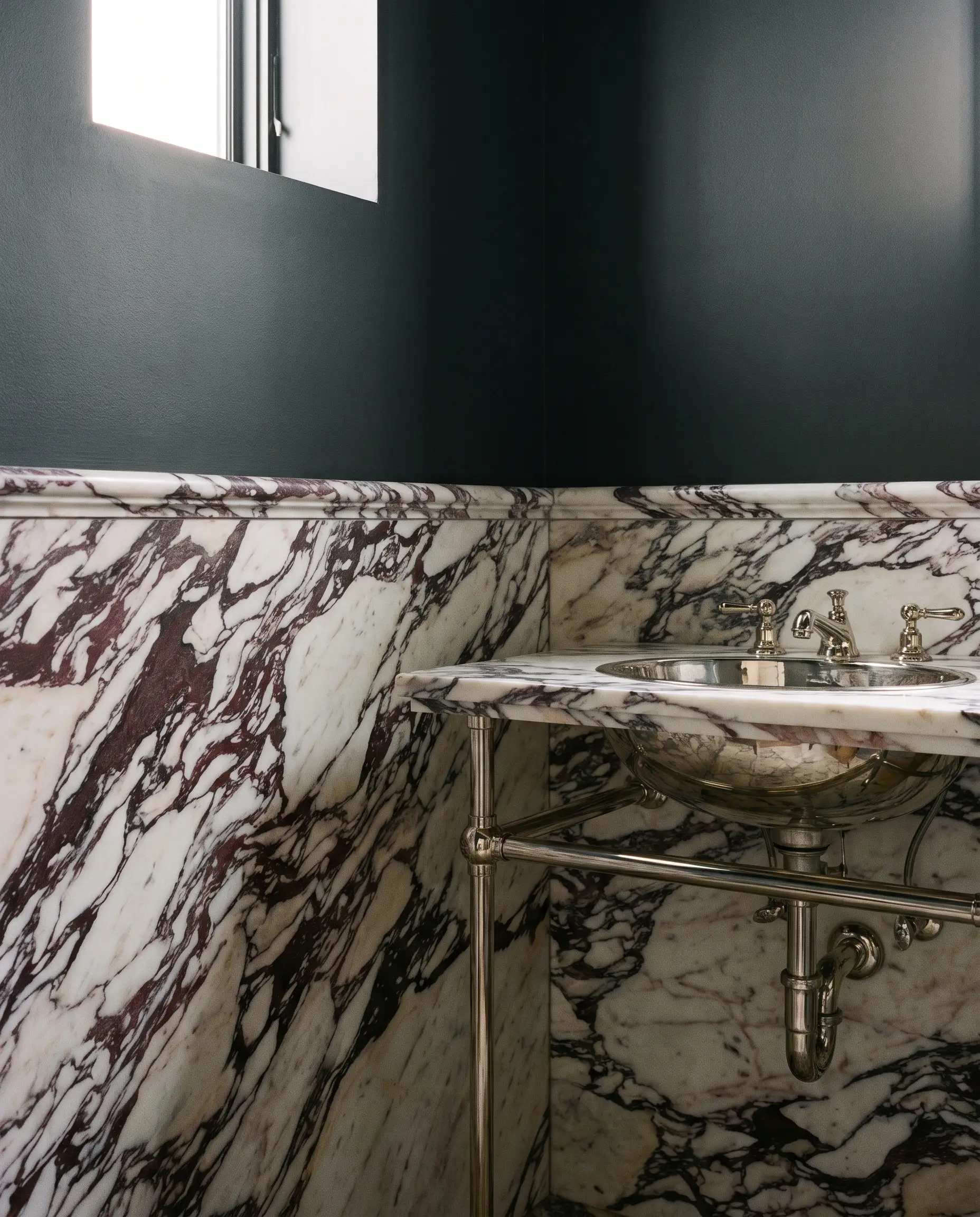 Luxurious Calacatta Viola marble wainscoting wraps a compact powder room beneath deep matte charcoal walls and a classic polished nickel console sink.