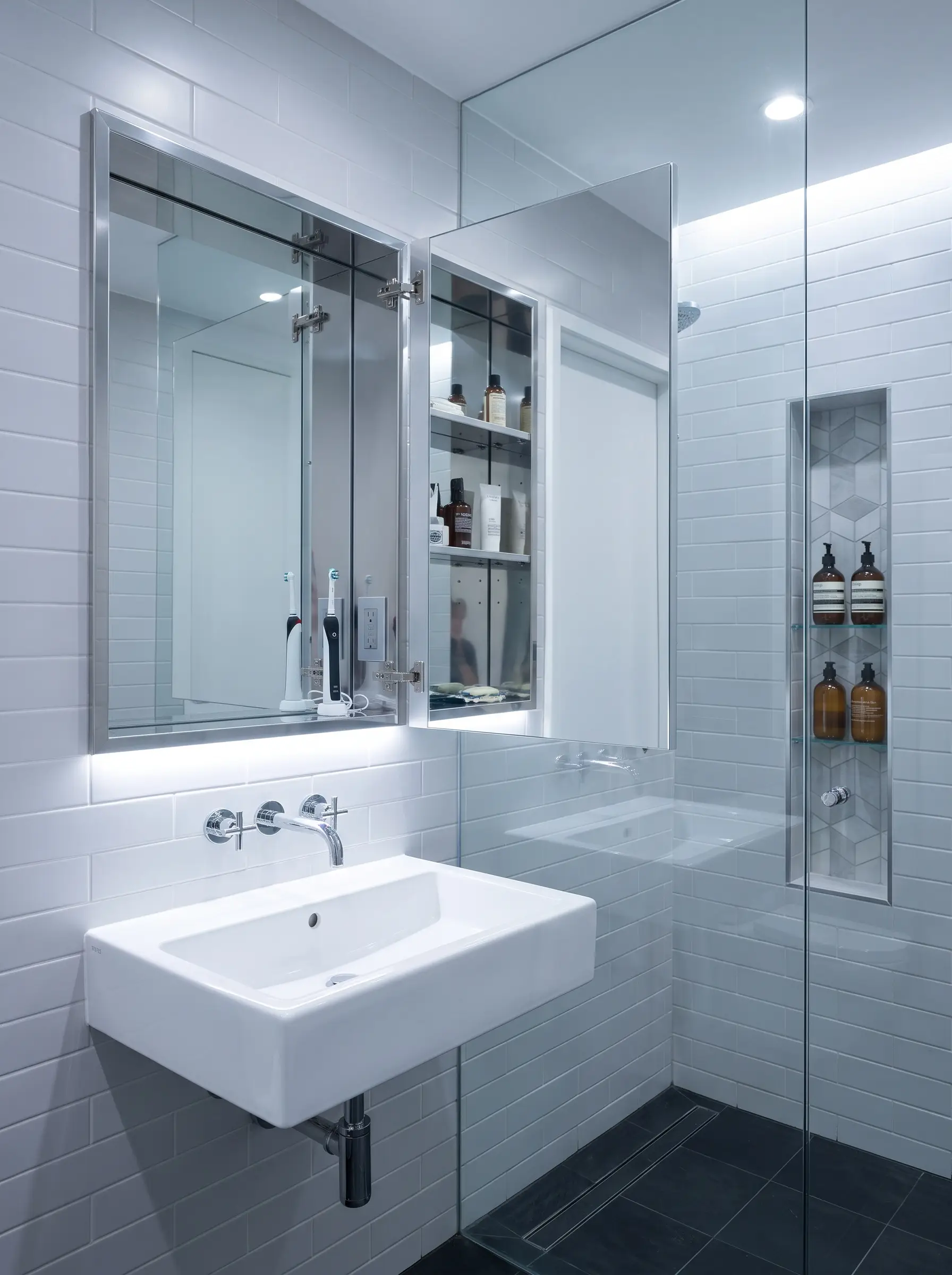 A highly efficient small bathroom design featuring a frameless recessed medicine cabinet, wall-mounted porcelain sink, and a custom-tiled shower wall niche.