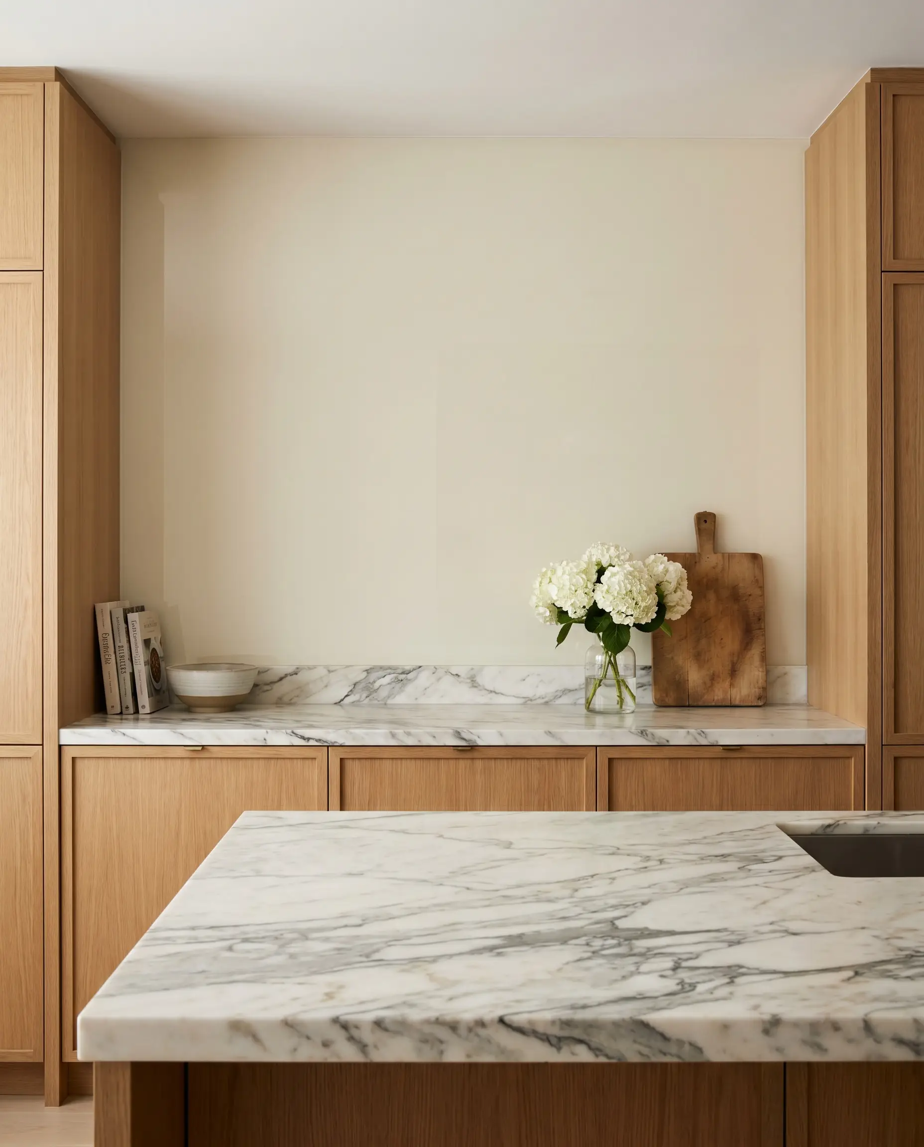 A quiet, solid back-painted glass vertical plane provides a minimalist backdrop to perfectly balance an aggressively patterned, heavily veined marble countertop in a luxury kitchen.