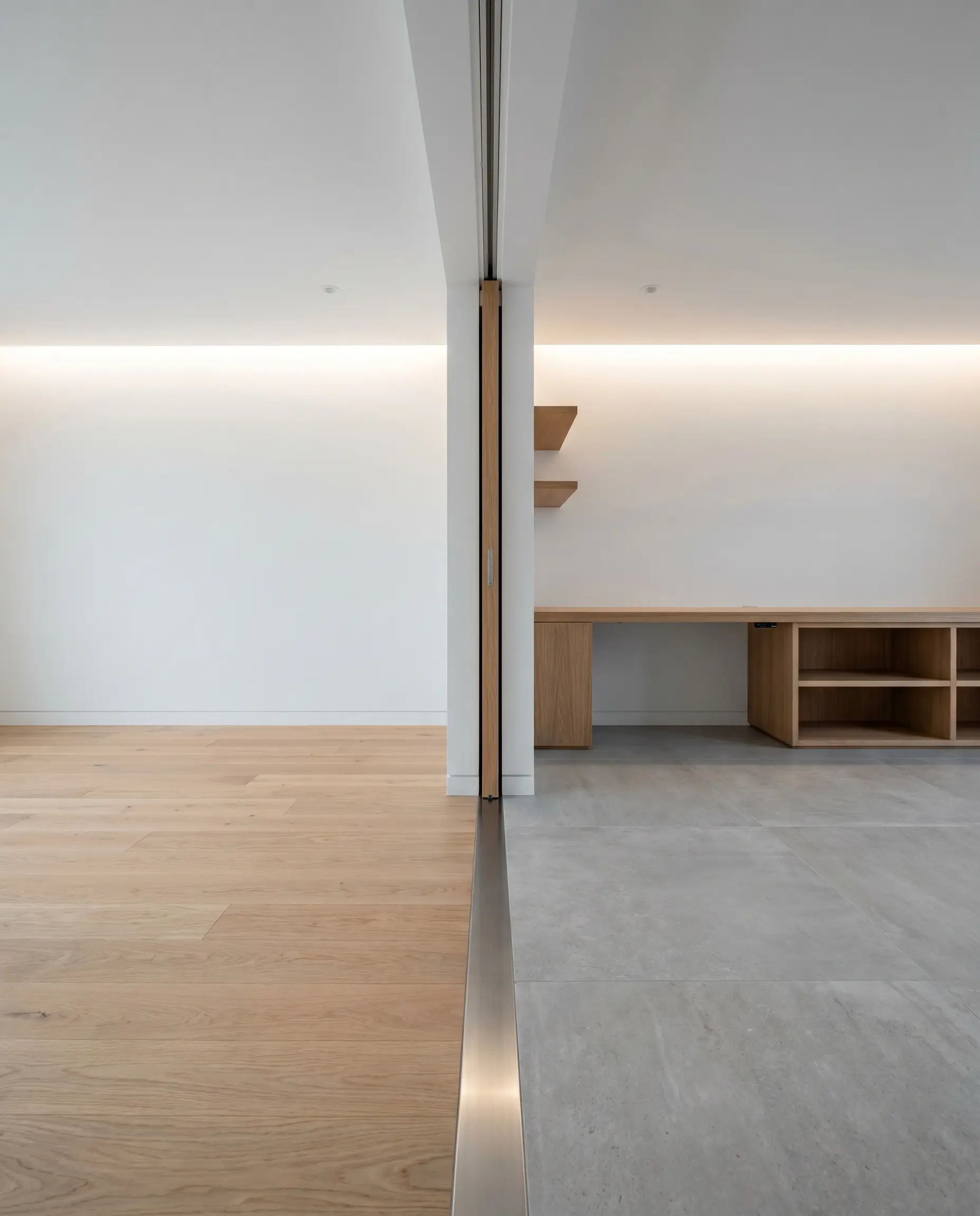 A stainless steel T-profile sits completely flush between wood and tile flooring, perfectly aligned underneath the center track of a concealed pocket door.