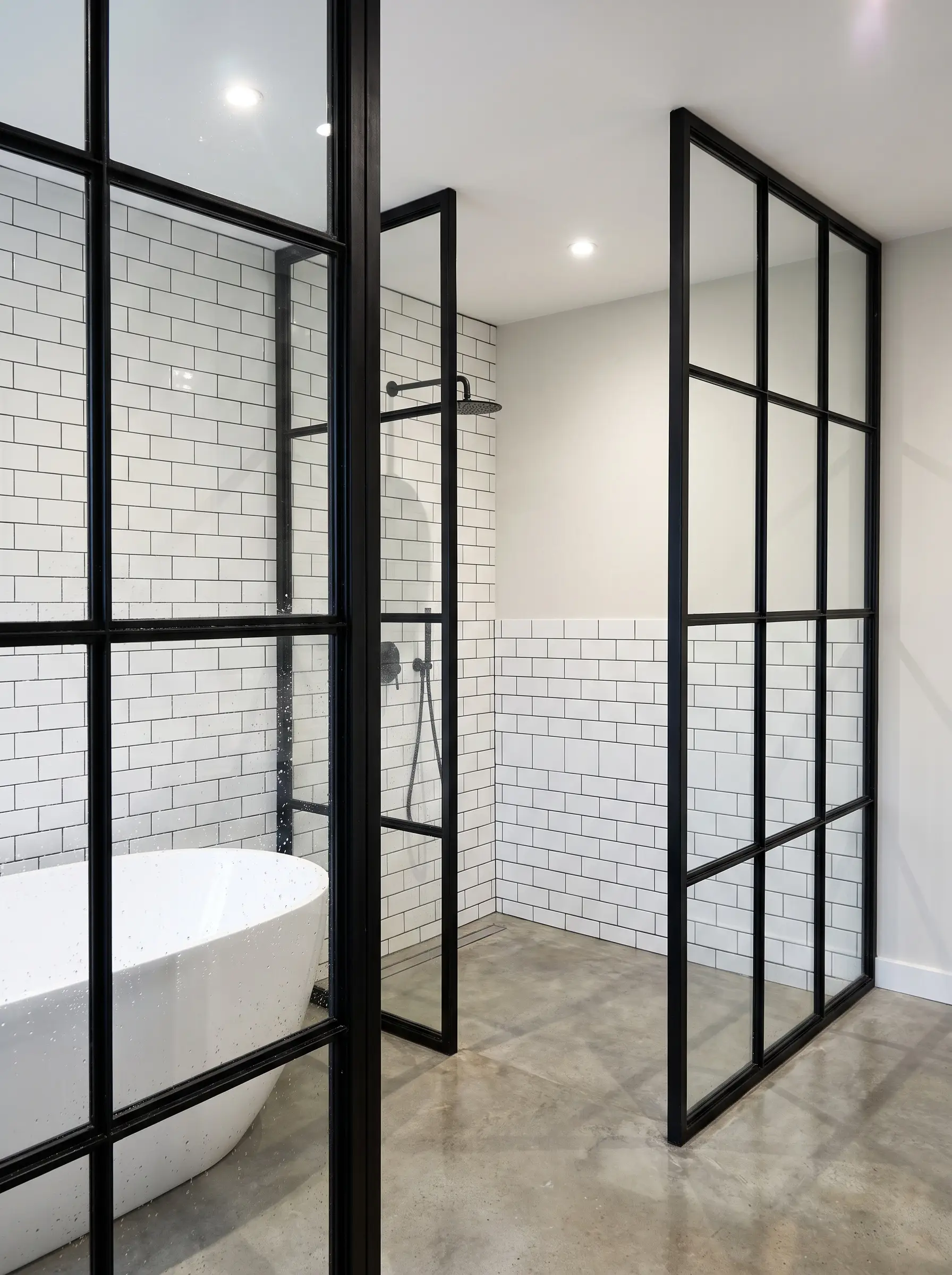 Bold black powder-coated stainless steel Crittall screens define a wet zone against Sherwin-Williams Pure White walls and crisp white subway tiles.