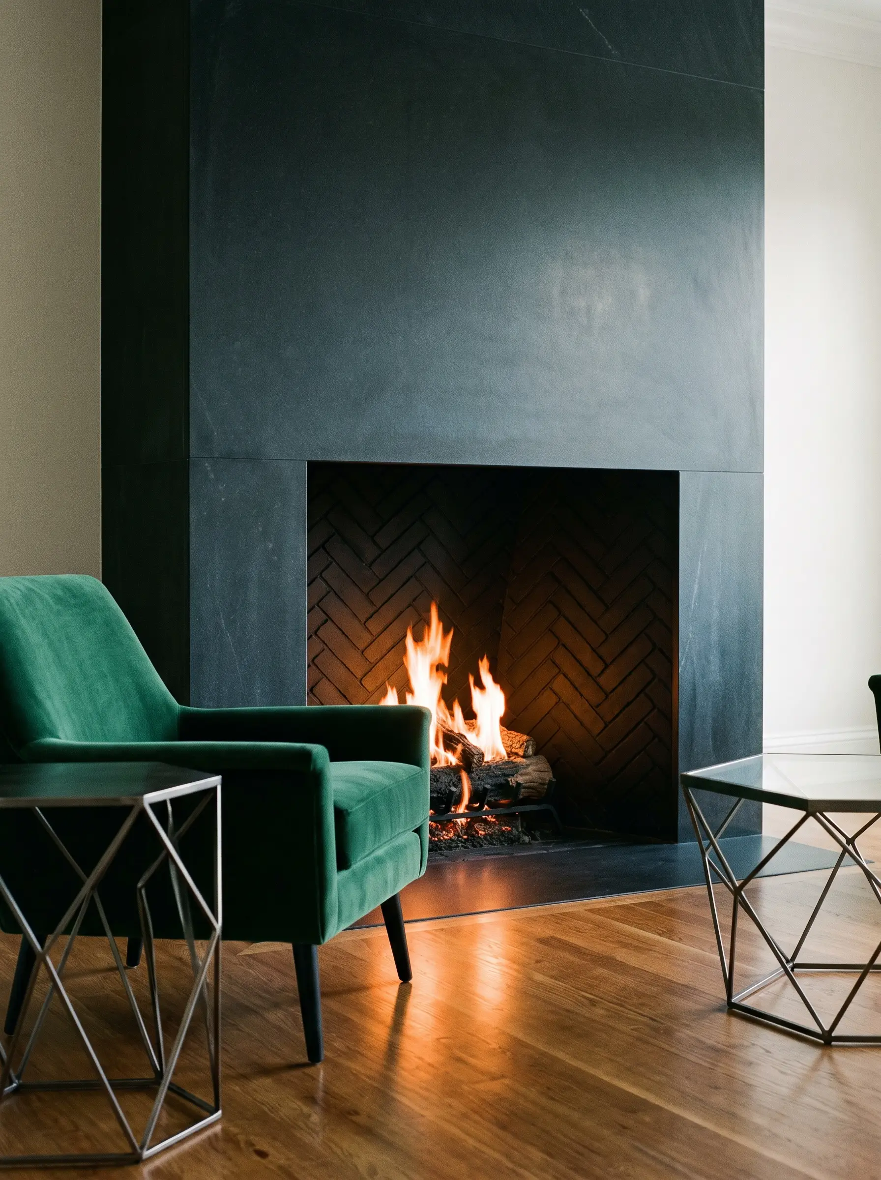 A modern minimalist interior firebox painted in flat Tricorn black enamel sits within a honed dark soapstone face beside a contemporary velvet accent chair.