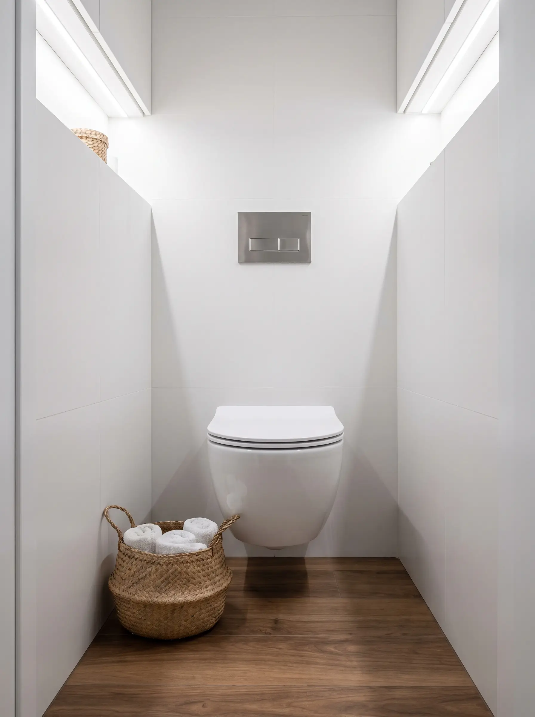 A sleek wall-hung toilet with a concealed cistern sits against a matte white tiled wall above walnut-toned porcelain wood-look flooring.