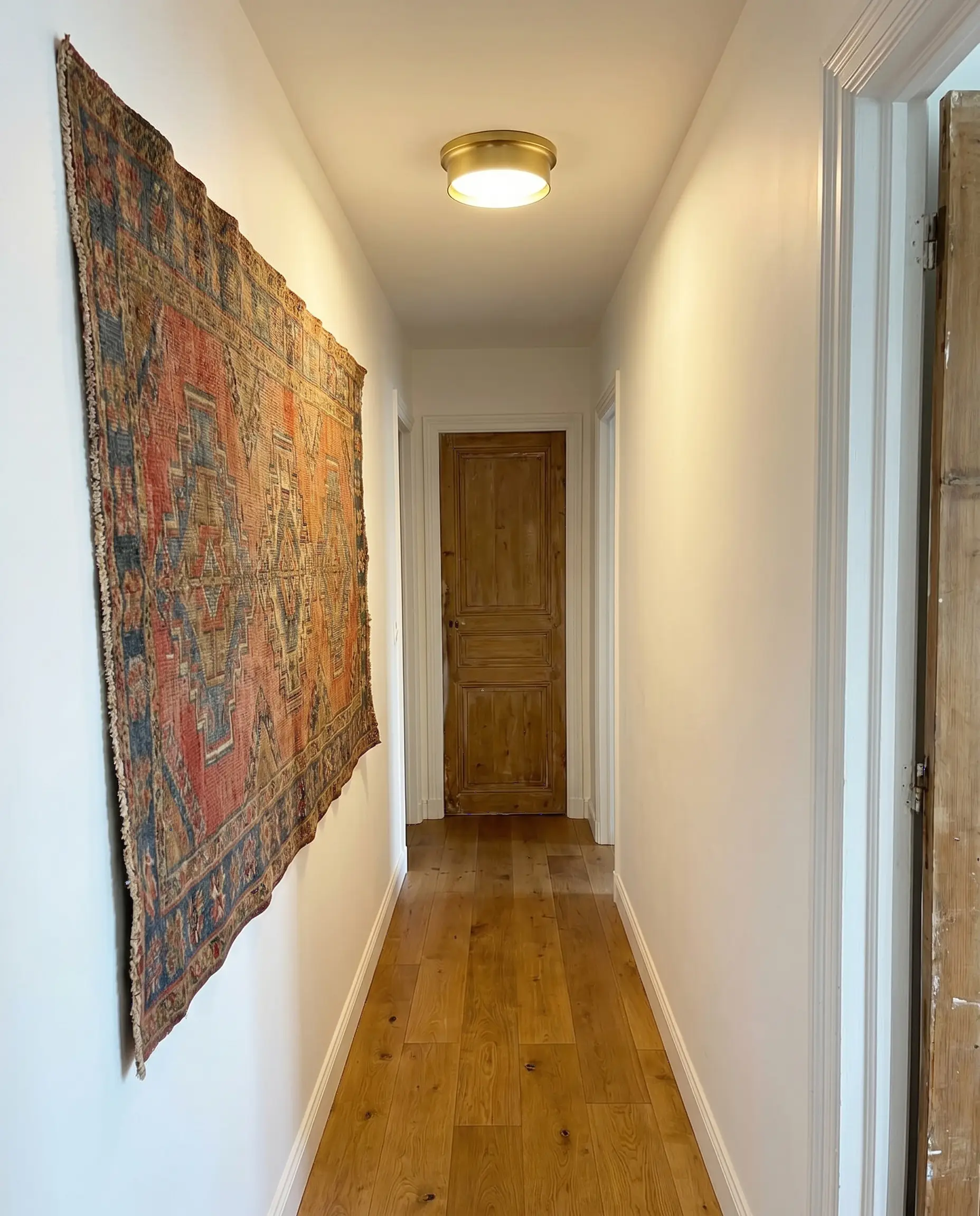 An unframed vintage kilim fragment hangs perfectly flat against crisp white drywall above a warm oak floor and simple flush-mount ceiling light.