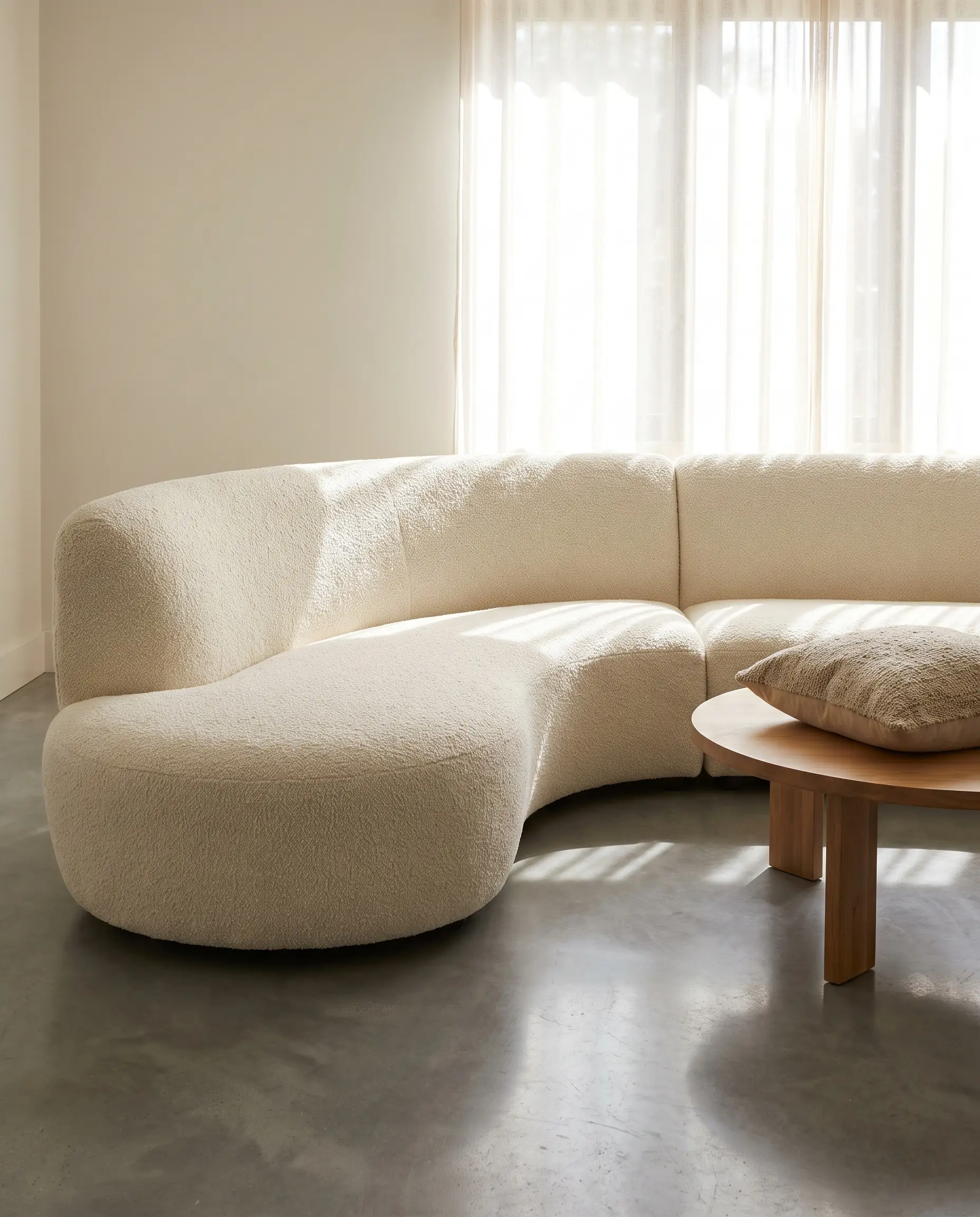 A massive warm-white shearling boucle sofa and round wooden coffee table soften the cool modern base of an inviting living room.